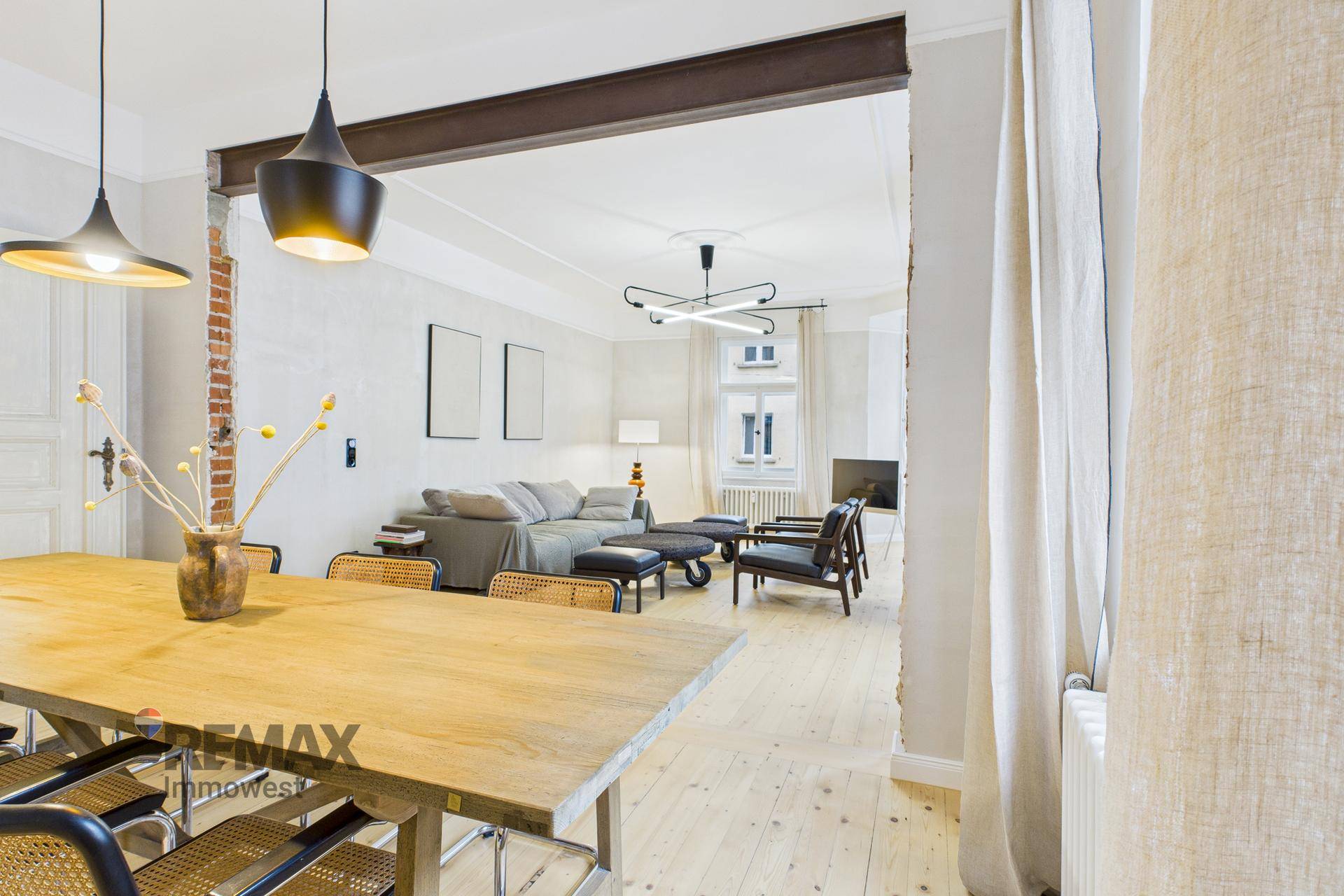 Blick vom Essbereich in den hellen Wohnbereich mit Sofa und modernen Leuchten.