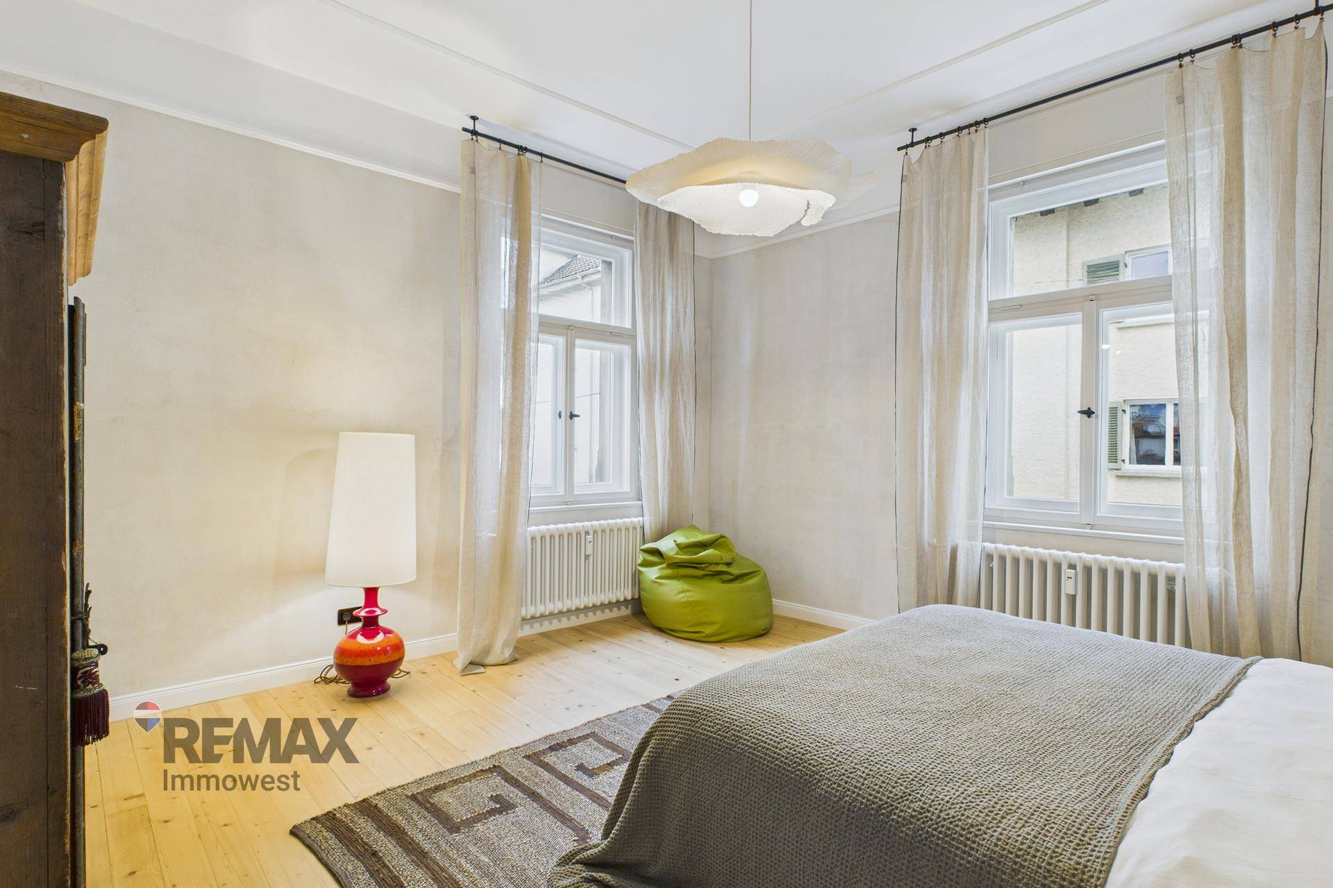 Helles Schlafzimmer mit zwei großen Fenstern, Holzboden und moderner Einrichtung.
