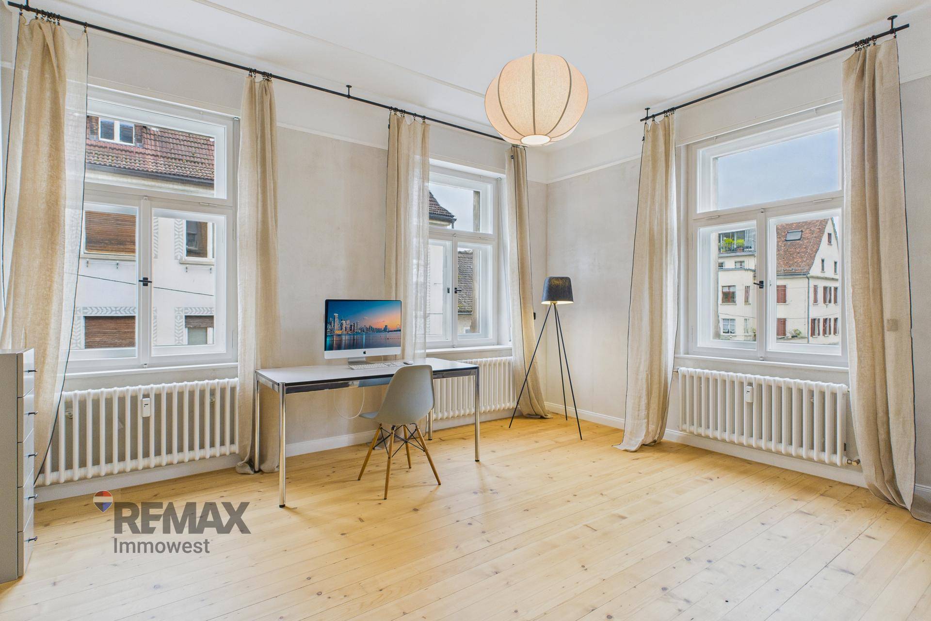 Helles Arbeitszimmer mit Holzboden, großen Fenstern und Blick nach draußen.