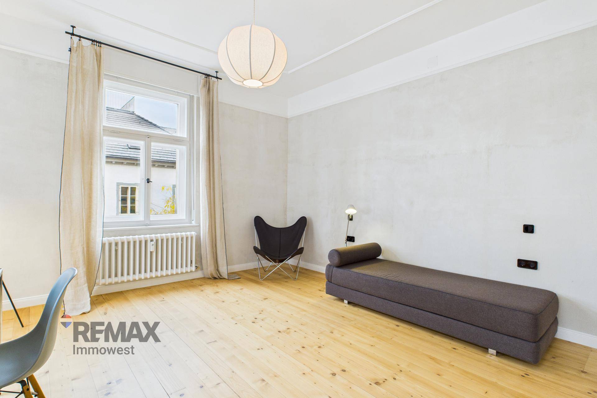 Ruhiger Raum mit Holzboden, Tagesliege und großem Fenster für entspannte Stunden.