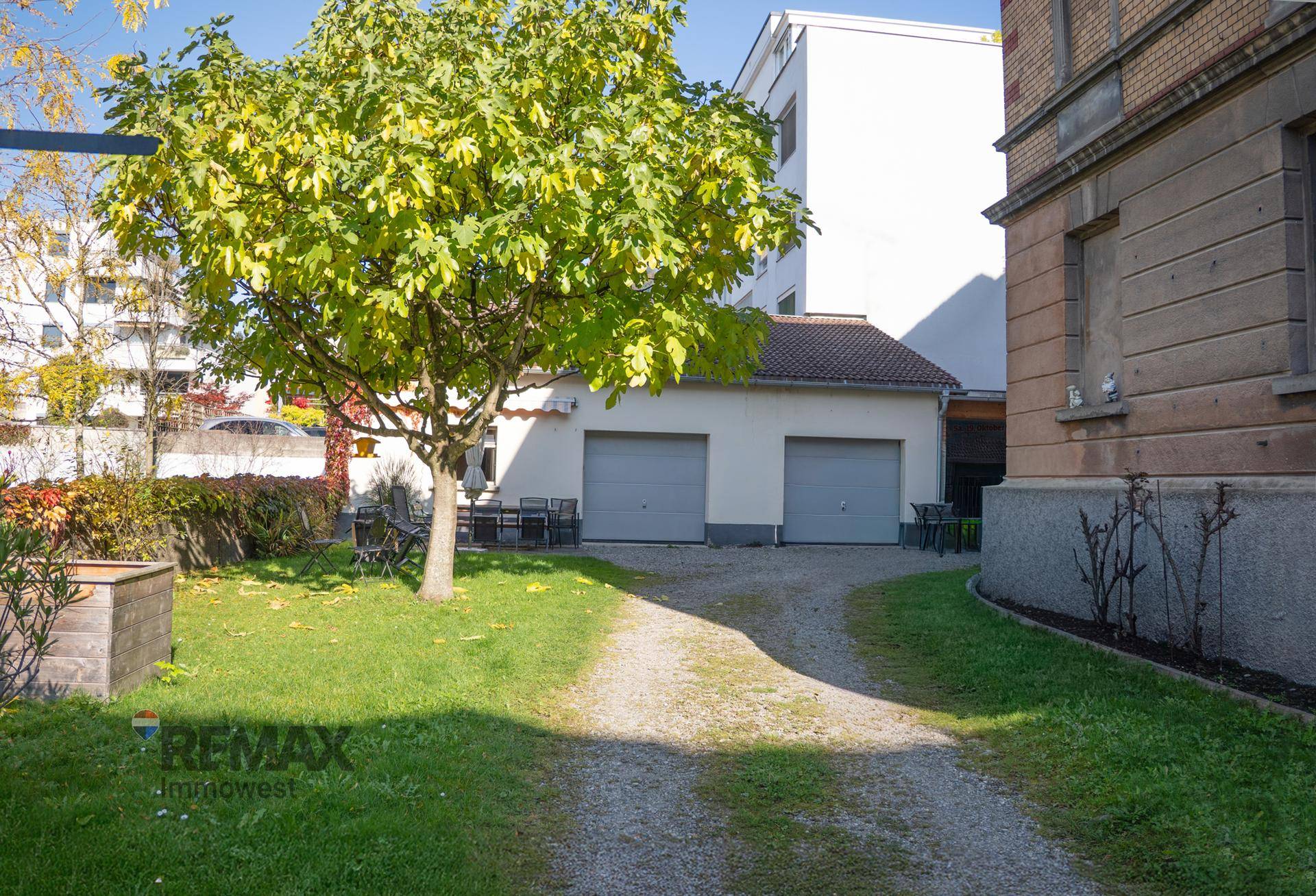 Grüner Gartenbereich mit Bäumen, Rasenfläche, Sitzgelegenheiten und Garagen.