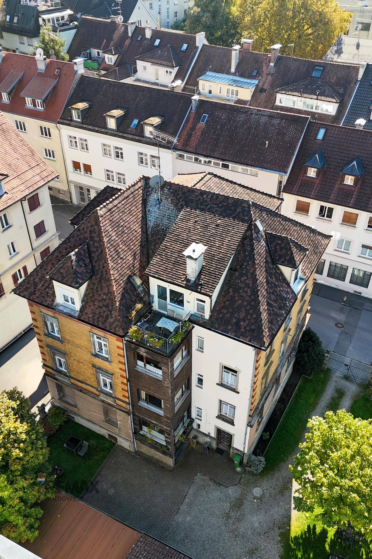 Luftaufnahme des Gebäudes mit markanter Dachlandschaft und umliegenden Häusern.