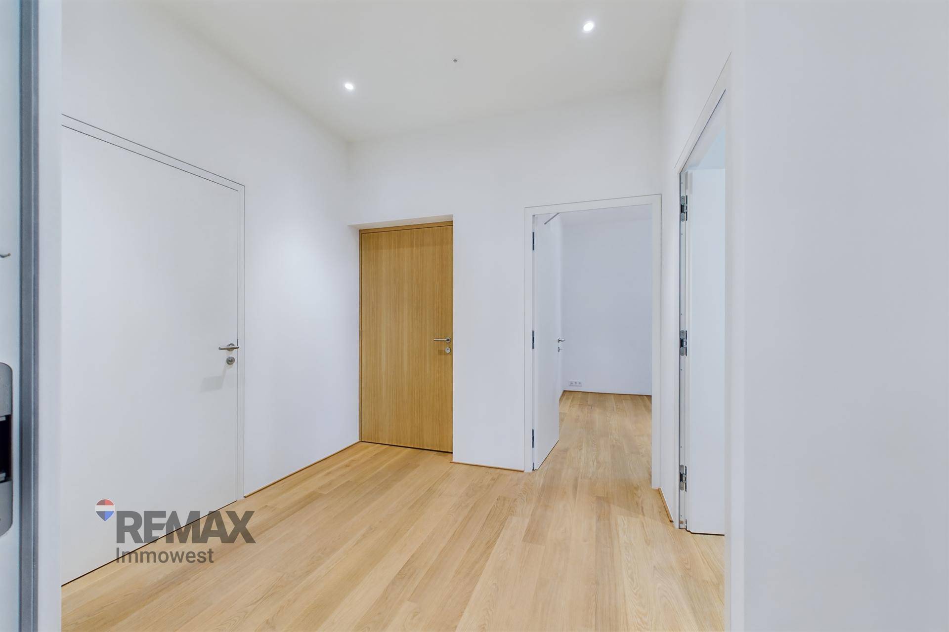 Geräumiger Flur mit hellem Holzboden und modernen weißen Türen in einem Neubau.