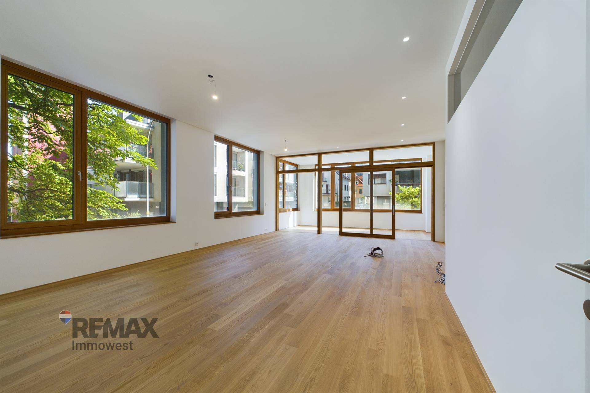 Geräumiger Wohnbereich mit Holzboden, großen Fenstern und einer eleganten Glasabtrennung.