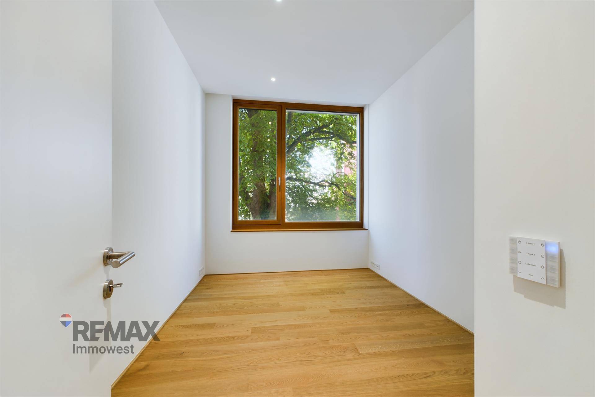 Gemütliches Zimmer mit Holzboden, weißer Wandfarbe und Fenster mit Blick auf Bäume.
