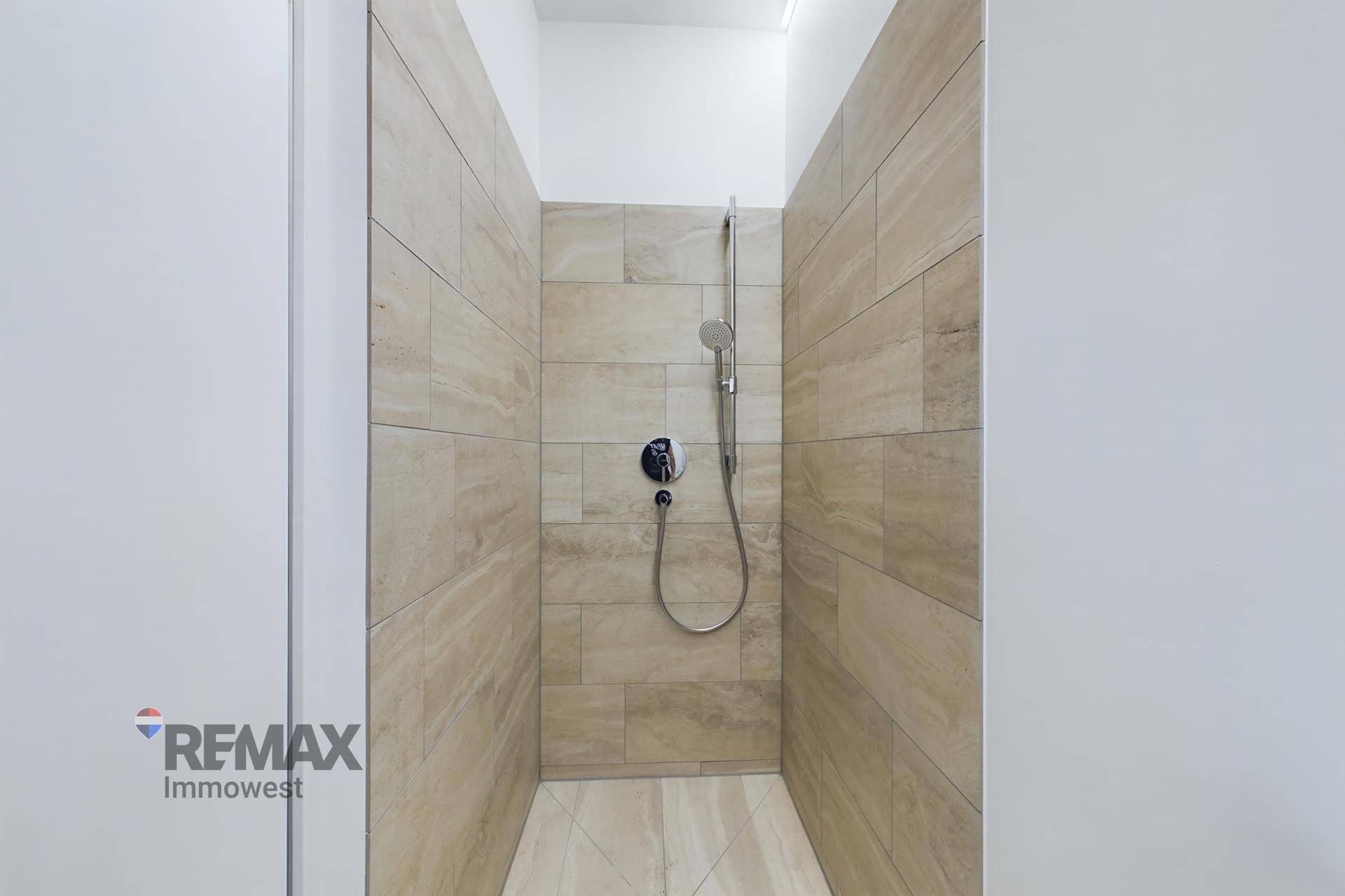Geräumige begehbare Dusche mit beigefarbenen Fliesen und moderner Regendusche.