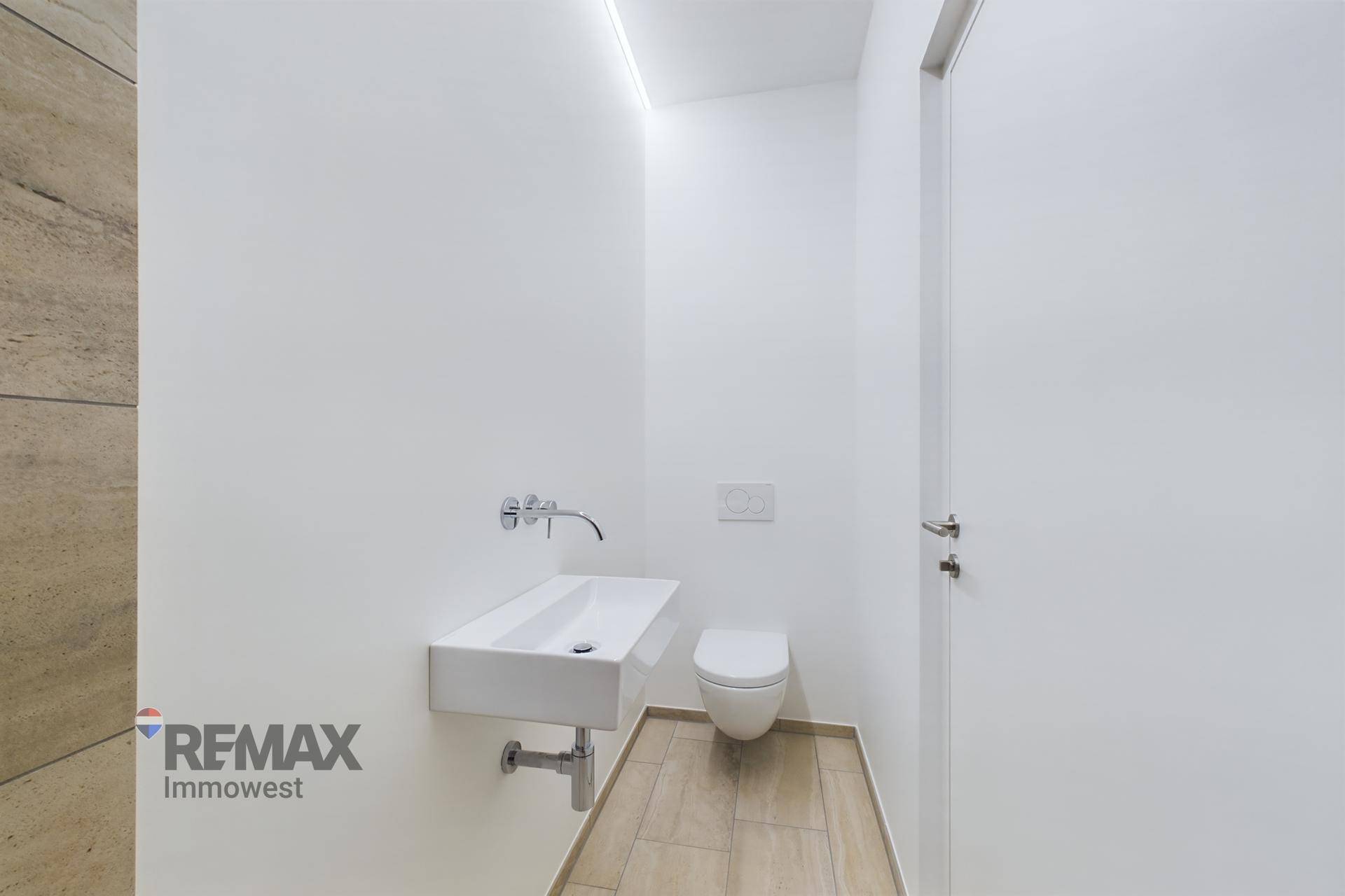 Modernes Gäste-WC mit wandhängender Toilette und kleinem Waschbecken, hell gefliest.