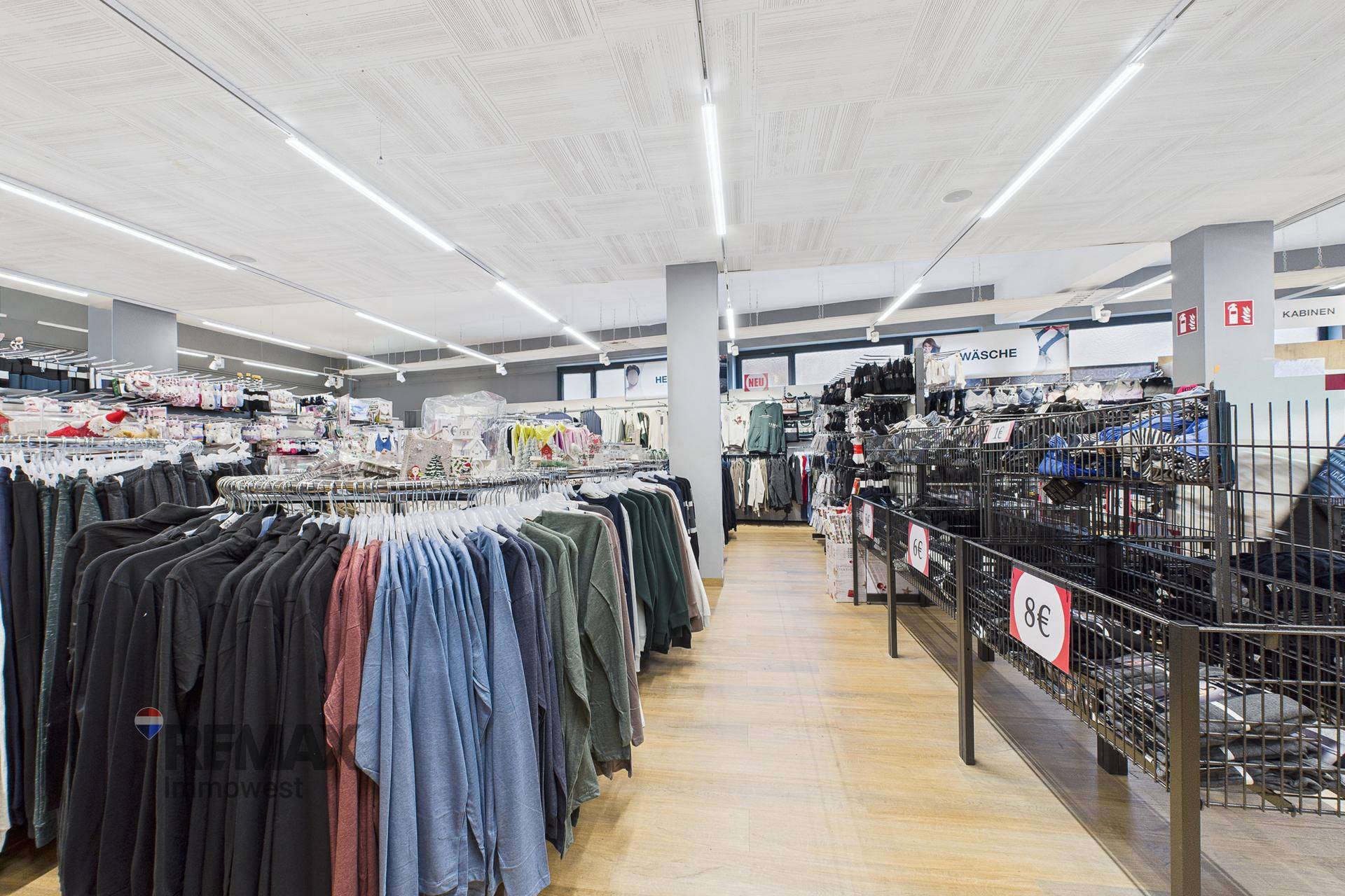 Weitläufiger Verkaufsbereich mit zahlreichen Kleiderständern und Hinweisschildern für Umkleidekabinen.