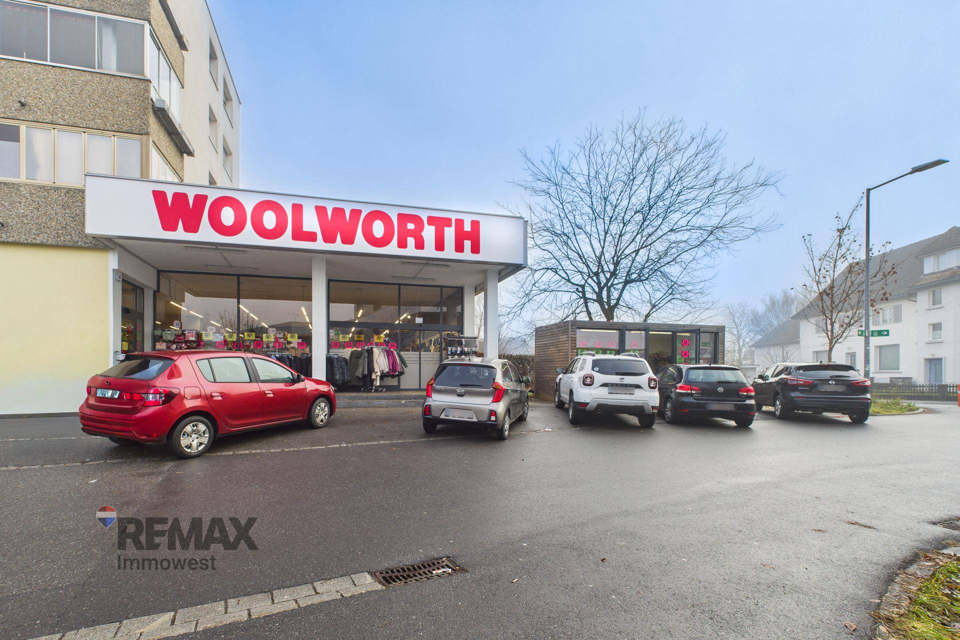 Außenansicht des Woolworth-Geschäfts mit Parkplätzen davor und umliegenden Gebäuden.