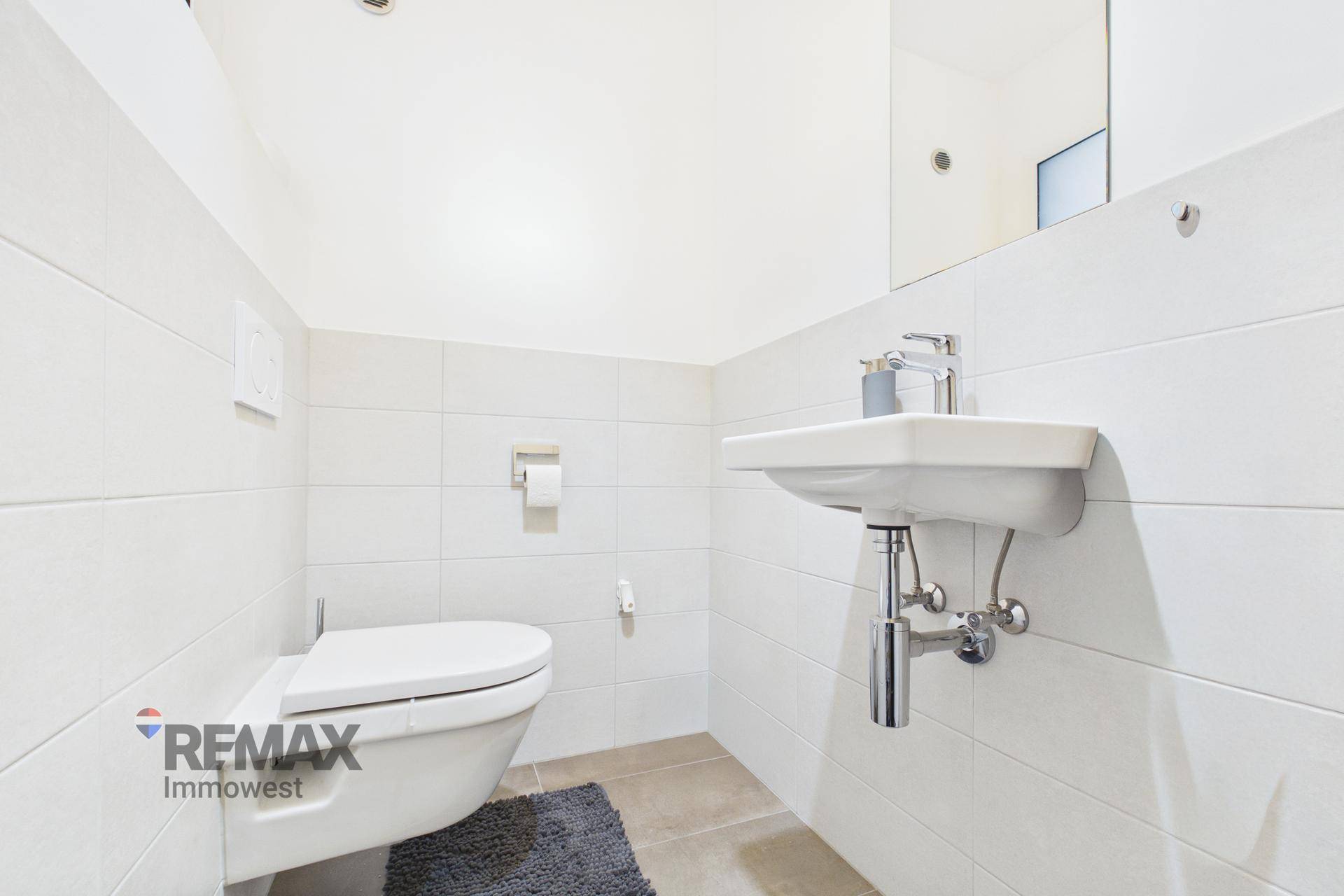 Modernes Gäste-WC mit weißen Fliesen, Wand-WC und Waschbecken.