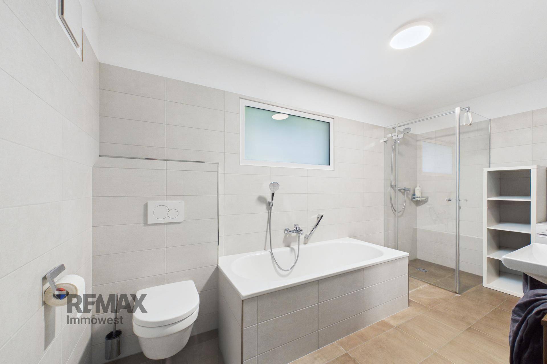 Modernes Badezimmer mit Badewanne, Dusche, Wand-WC und Fenster.