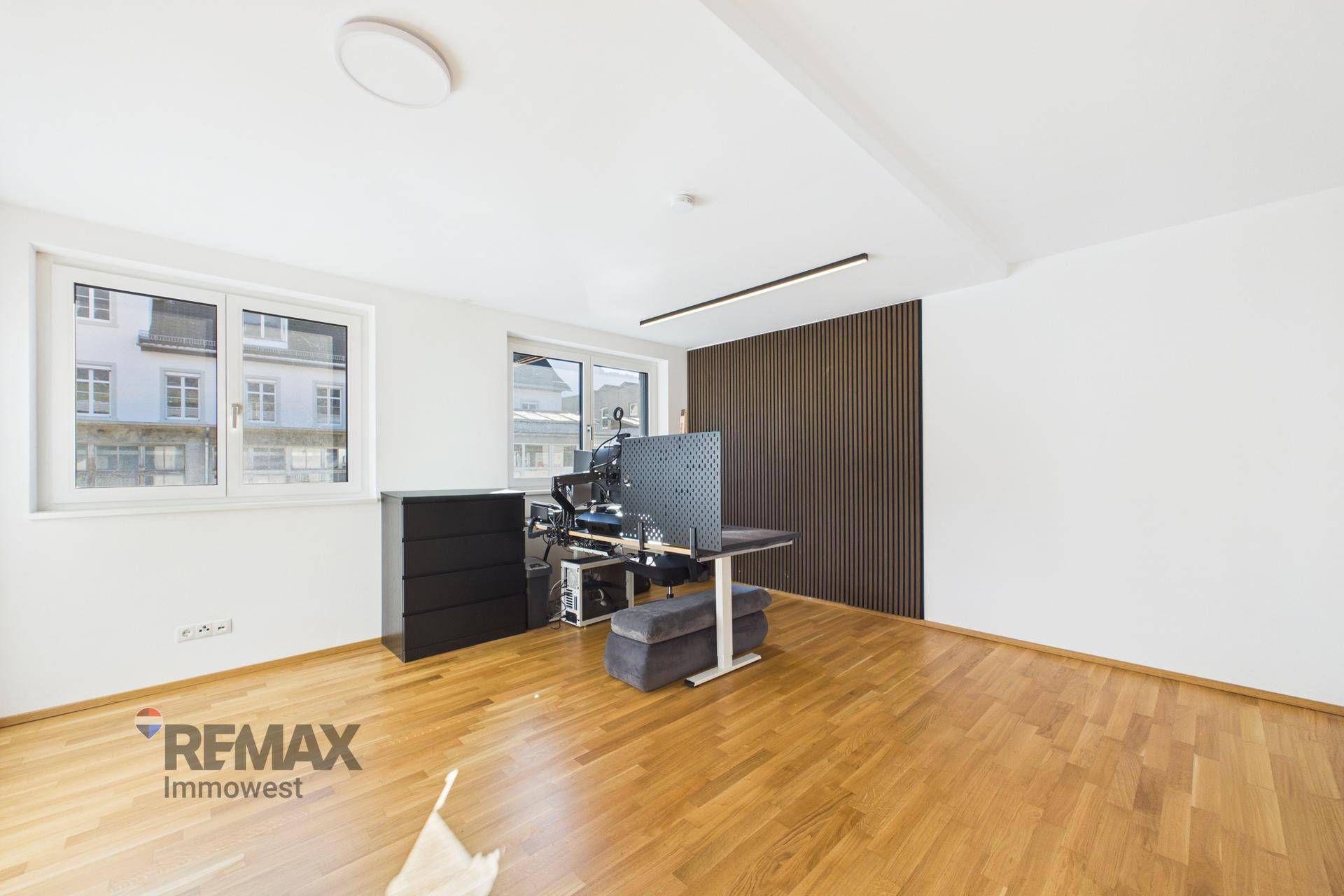 Geräumiges Büro mit Holzfußboden, großen Fenstern und moderner Wandverkleidung.