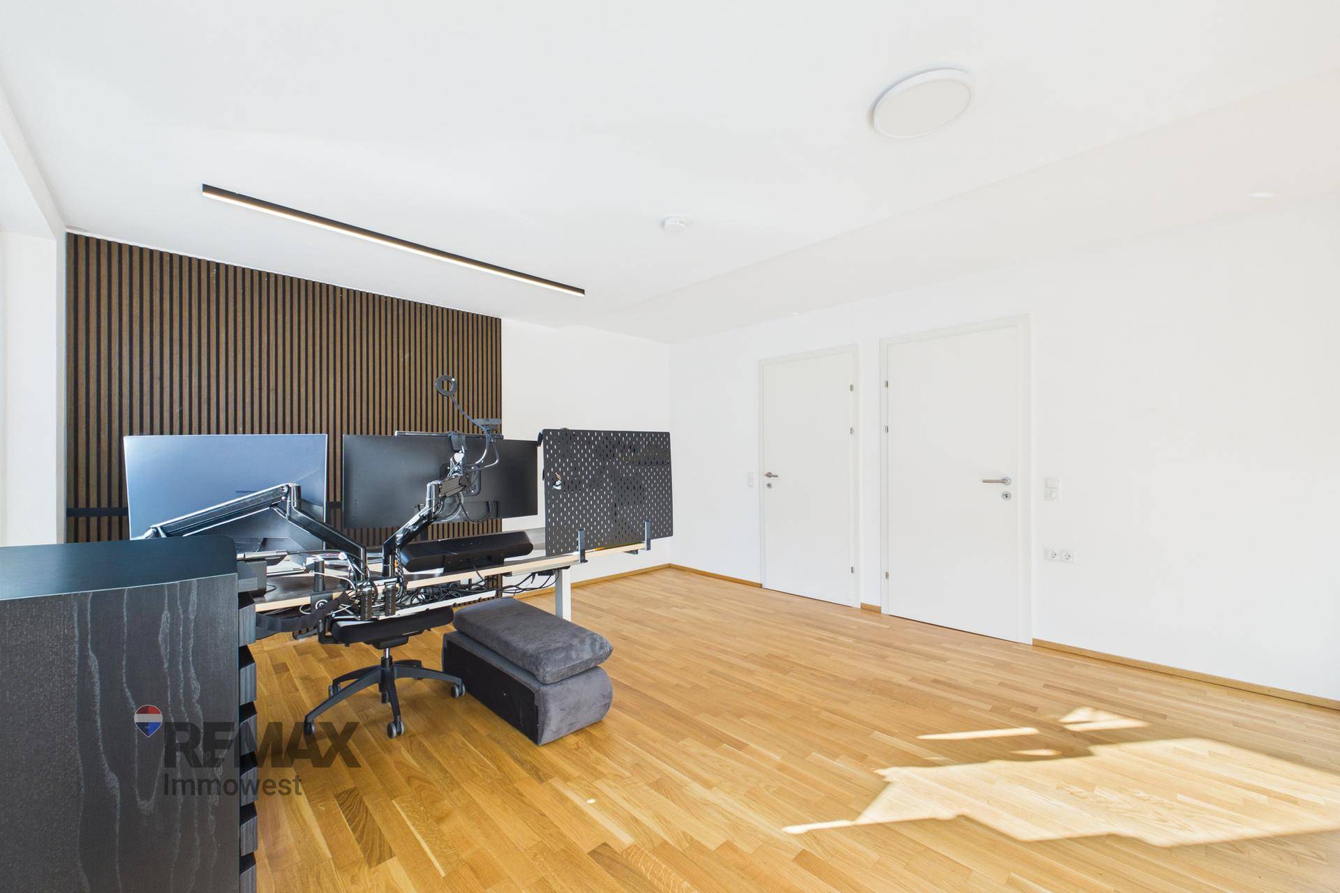 Helles Arbeitszimmer mit Holzfußboden, mehreren Monitoren und weißen Türen.