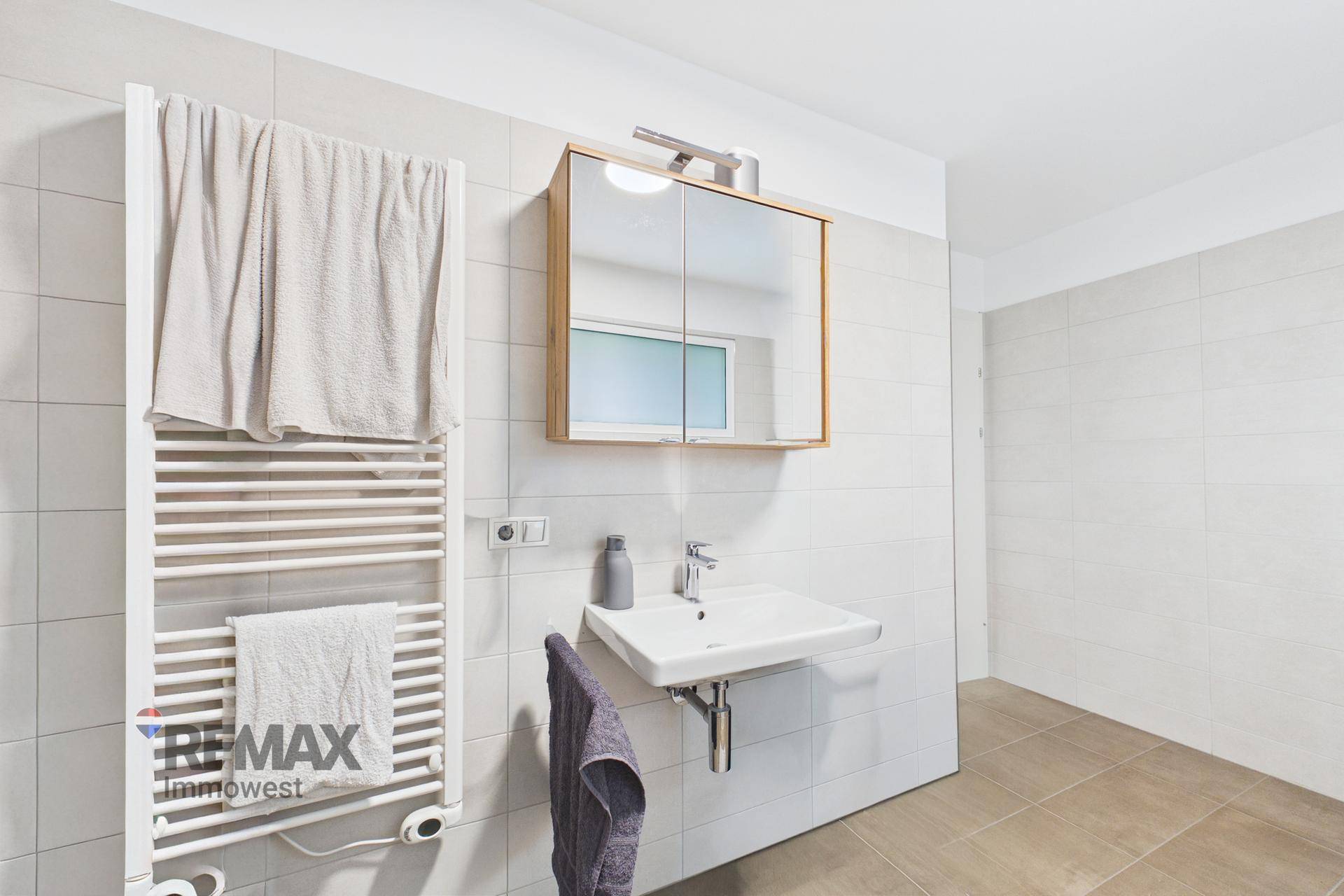 Helles Badezimmer mit Waschbecken, Spiegelschrank und beheiztem Handtuchhalter.