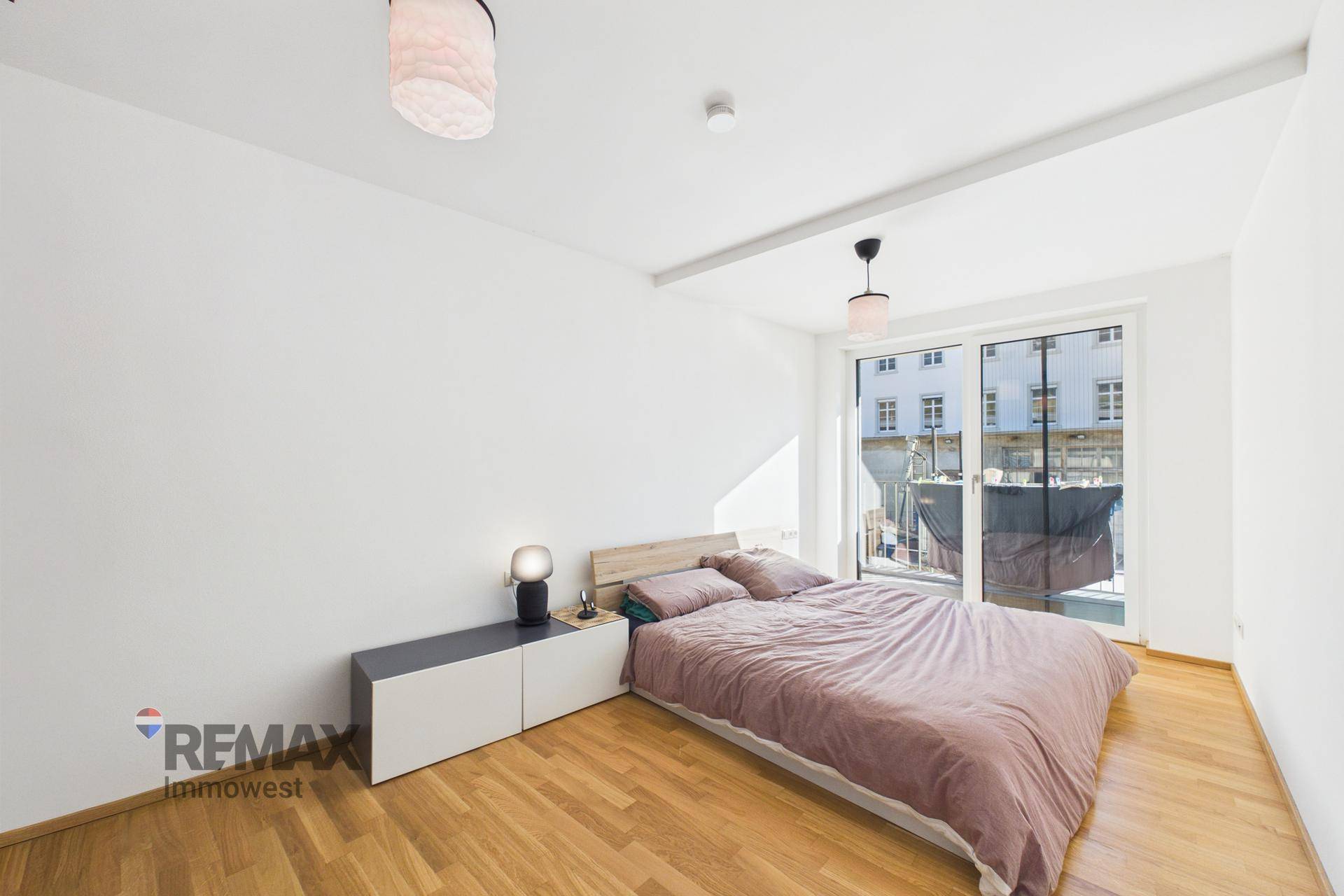 Helles Schlafzimmer mit Doppelbett, Holzfußboden und direktem Zugang zum Balkon.