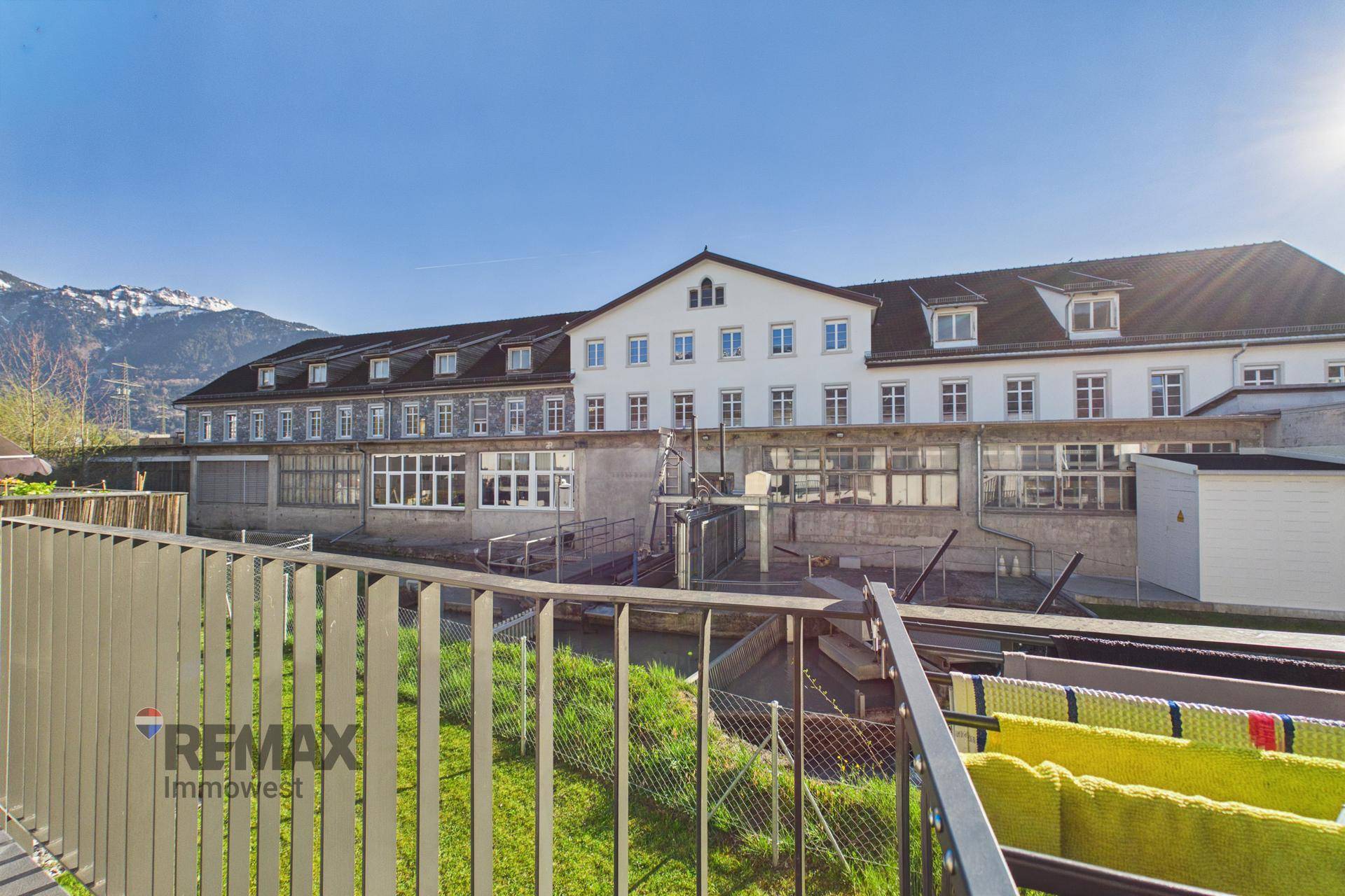 Balkon mit Blick auf ein historisches Gebäude, Berge und einen Bachlauf.