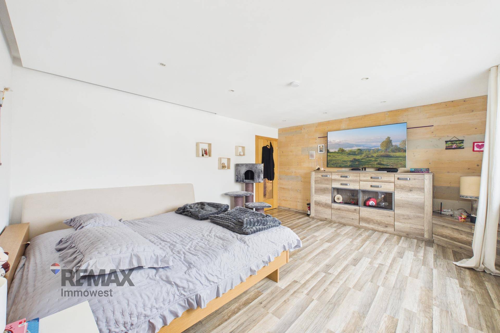 Schlafzimmer mit Holzakzentwand, großem Bett und einem Medienmöbelstück mit Fernseher.