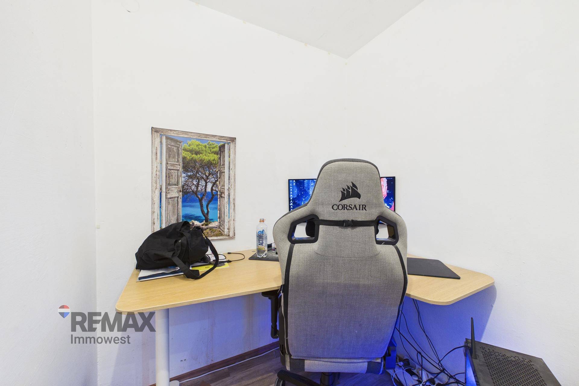 Funktionaler Arbeitsbereich mit Gaming-Stuhl, Schreibtisch und Computer-Setup in einem hellen Raum.