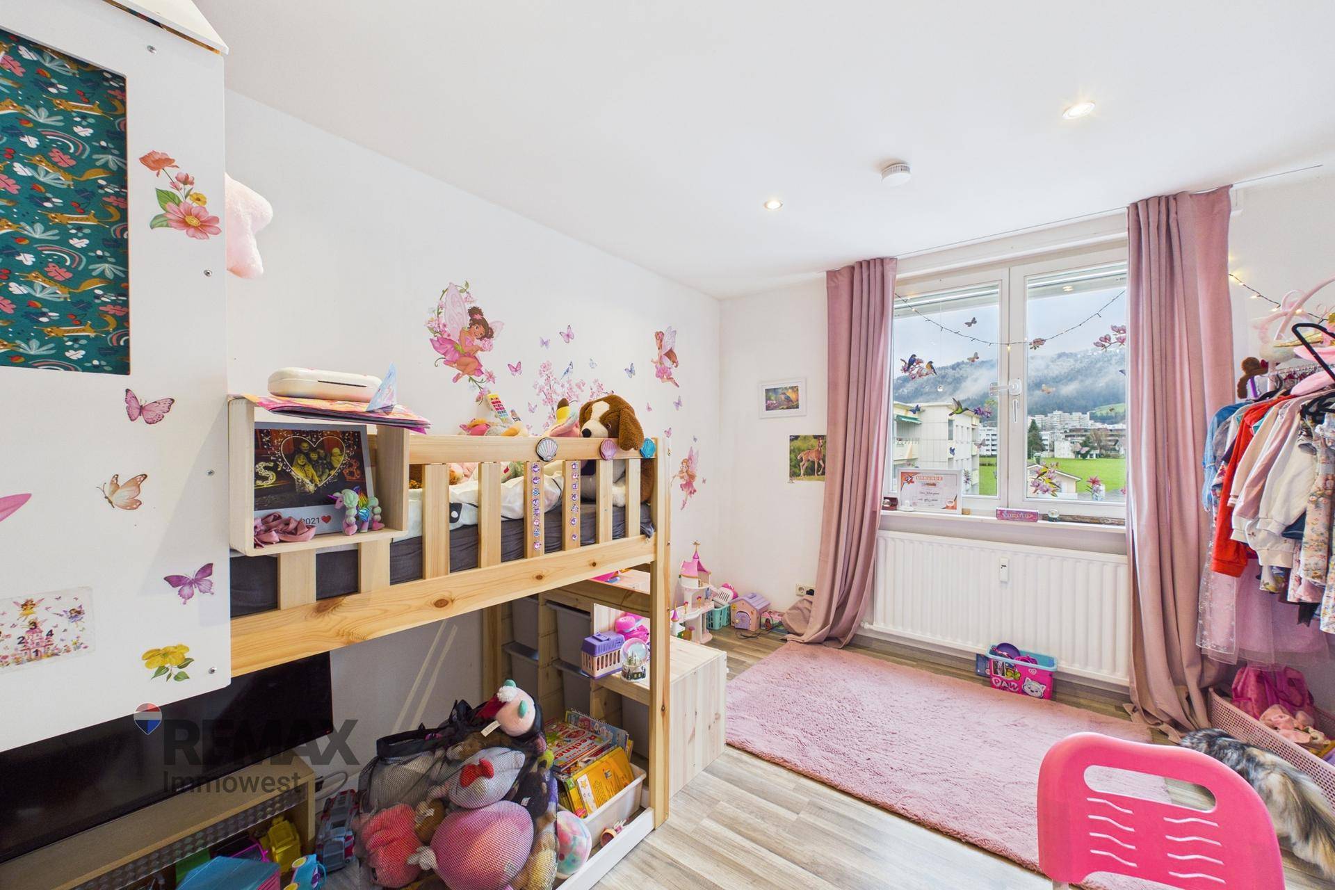 Kinderzimmer mit Etagenbett, rosa Teppich und verspielten Wanddekorationen, hell durch ein Fenster.
