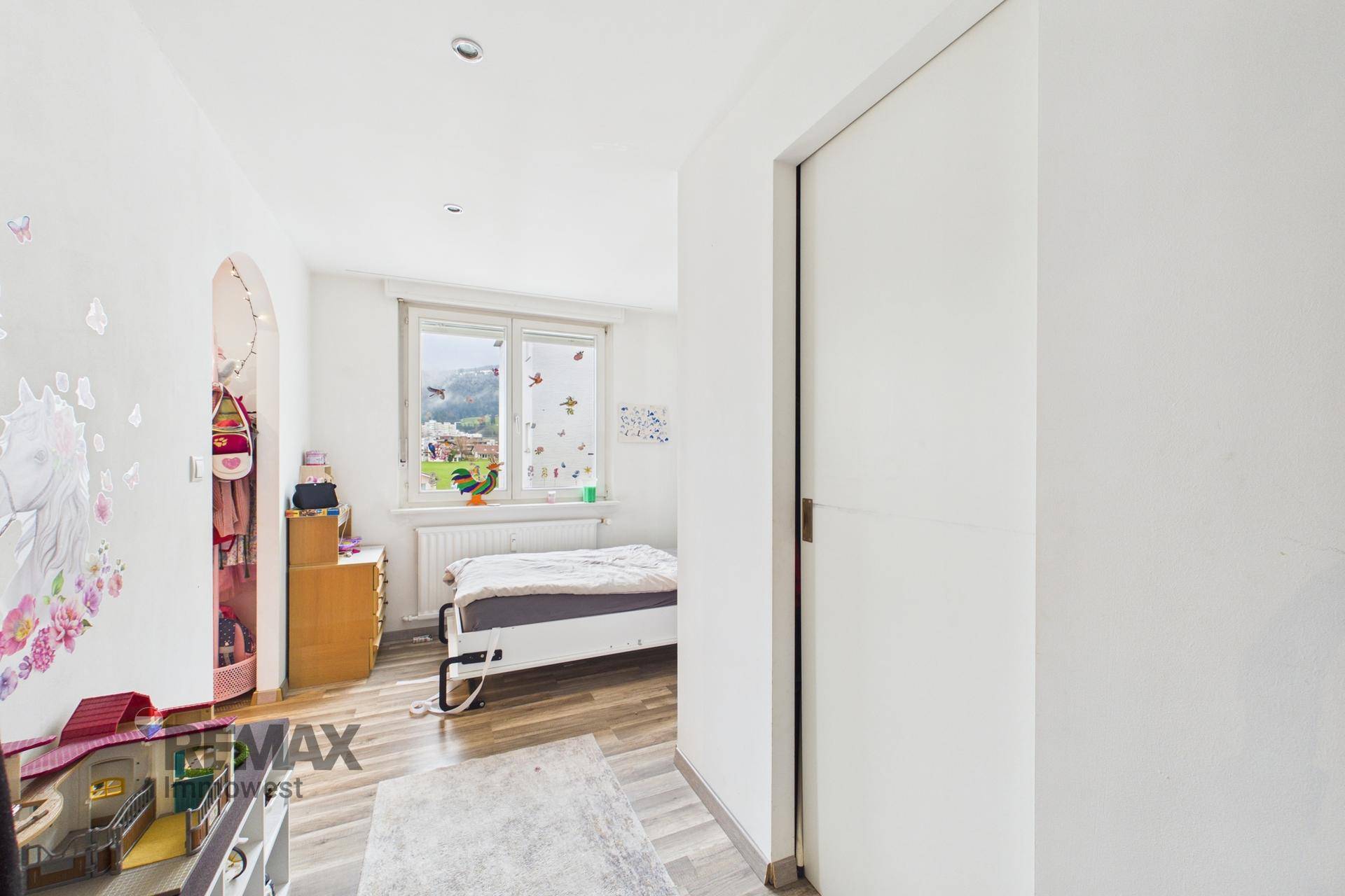 Helles Kinderzimmer mit Einzelbett, bunten Wandstickern und einem Fenster mit Ausblick.