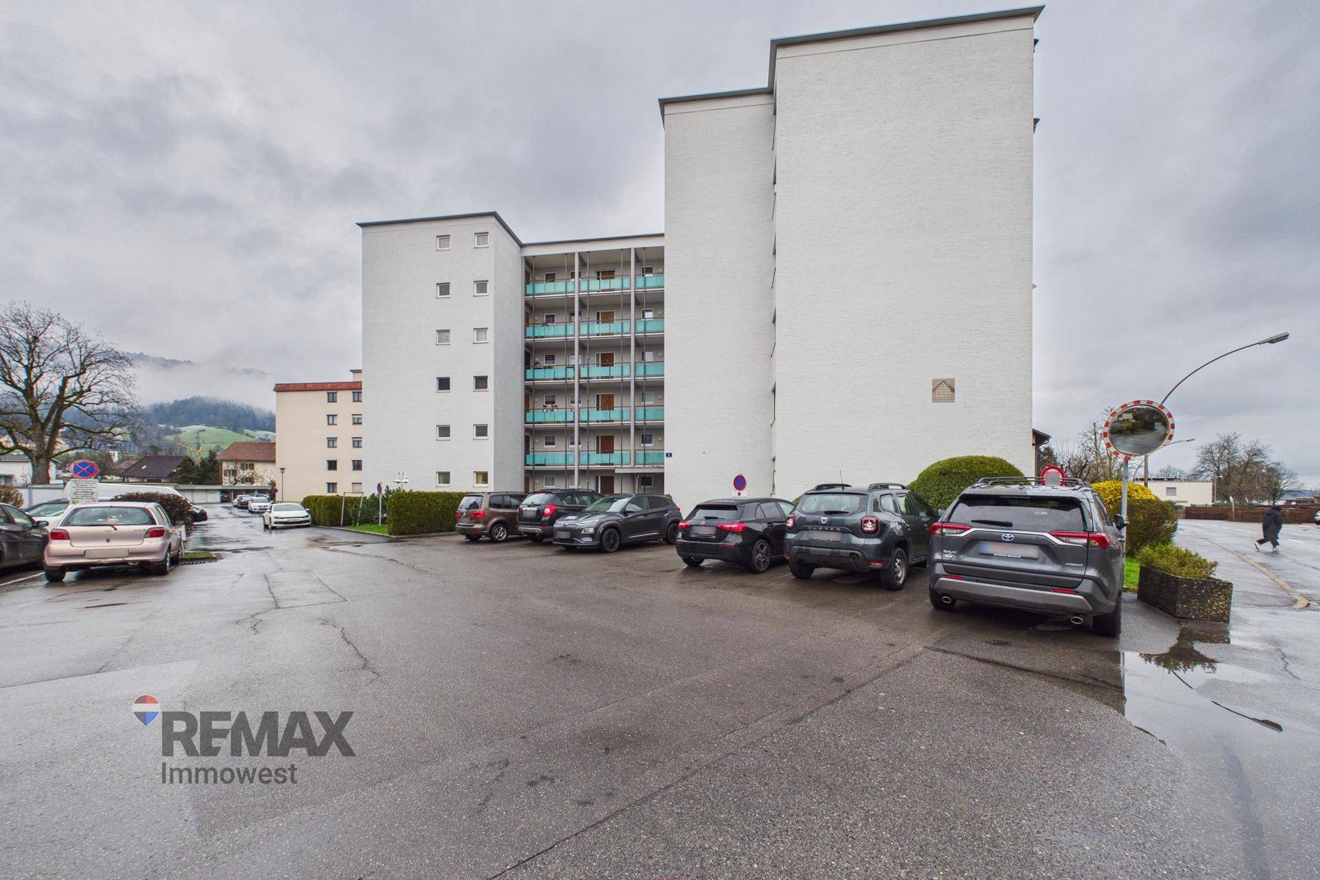 Ansicht des Wohngebäudes mit angrenzendem Parkplatz und weiteren Gebäuden im Hintergrund.
