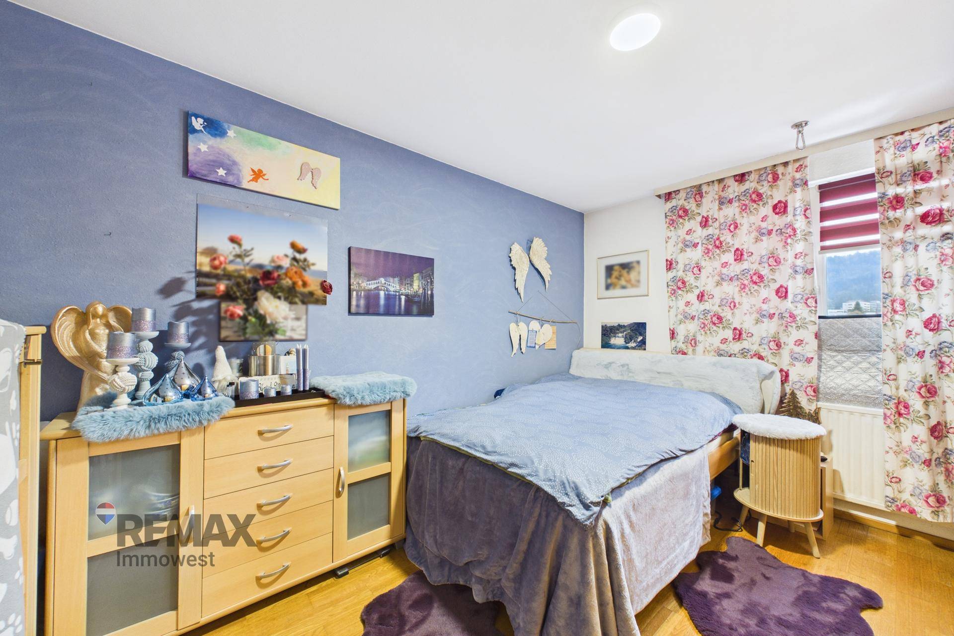 Schlafzimmer mit blauer Wand, Holzboden und einem Bett mit floraler Bettwäsche.