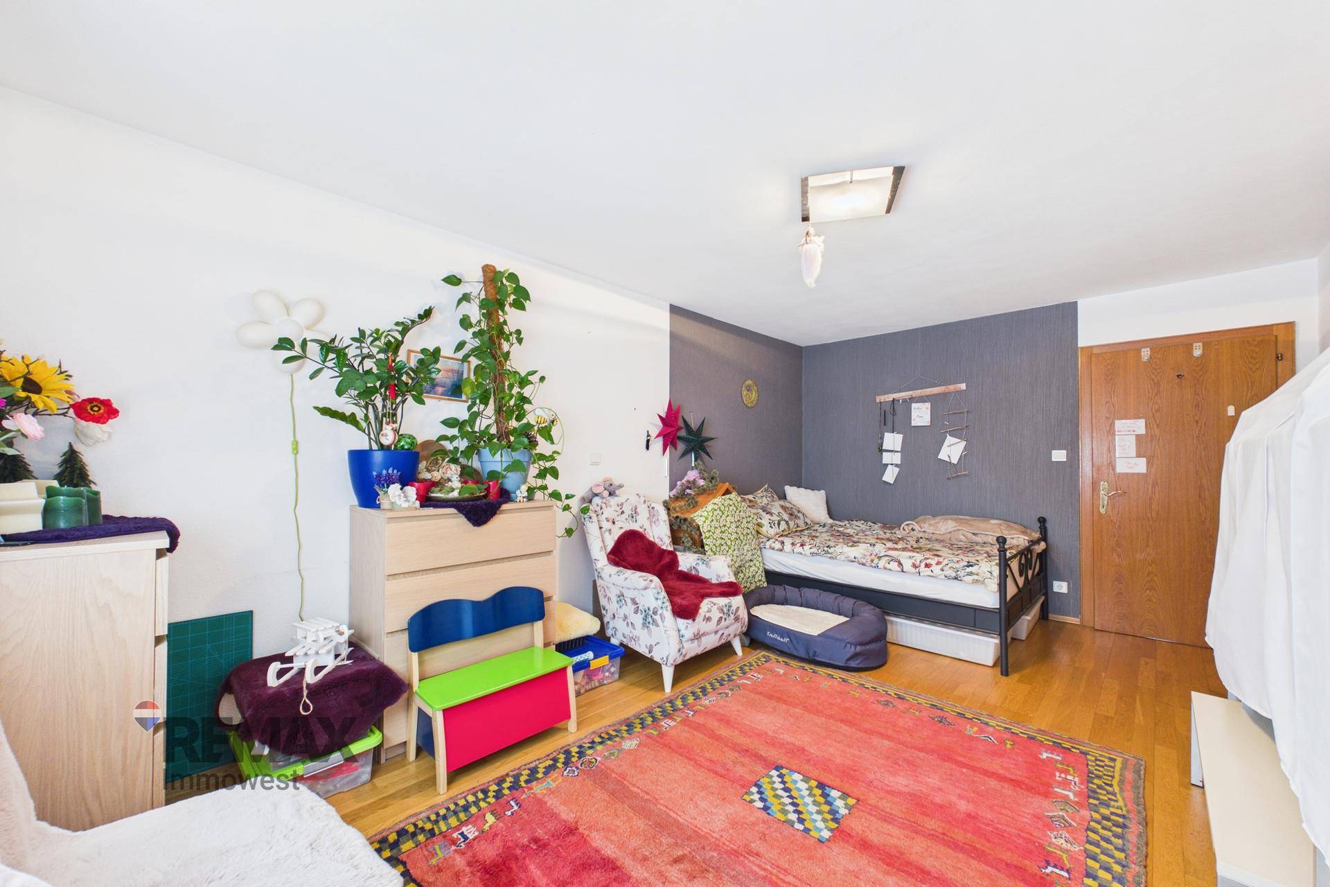 Schlafzimmer mit Holzboden, floralem Teppich und einem Bett mit Metallrahmen.
