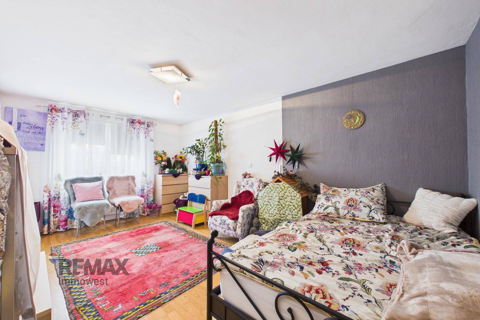 Geräumiges Schlafzimmer mit floraler Bettwäsche, Teppich und einem Sitzbereich.