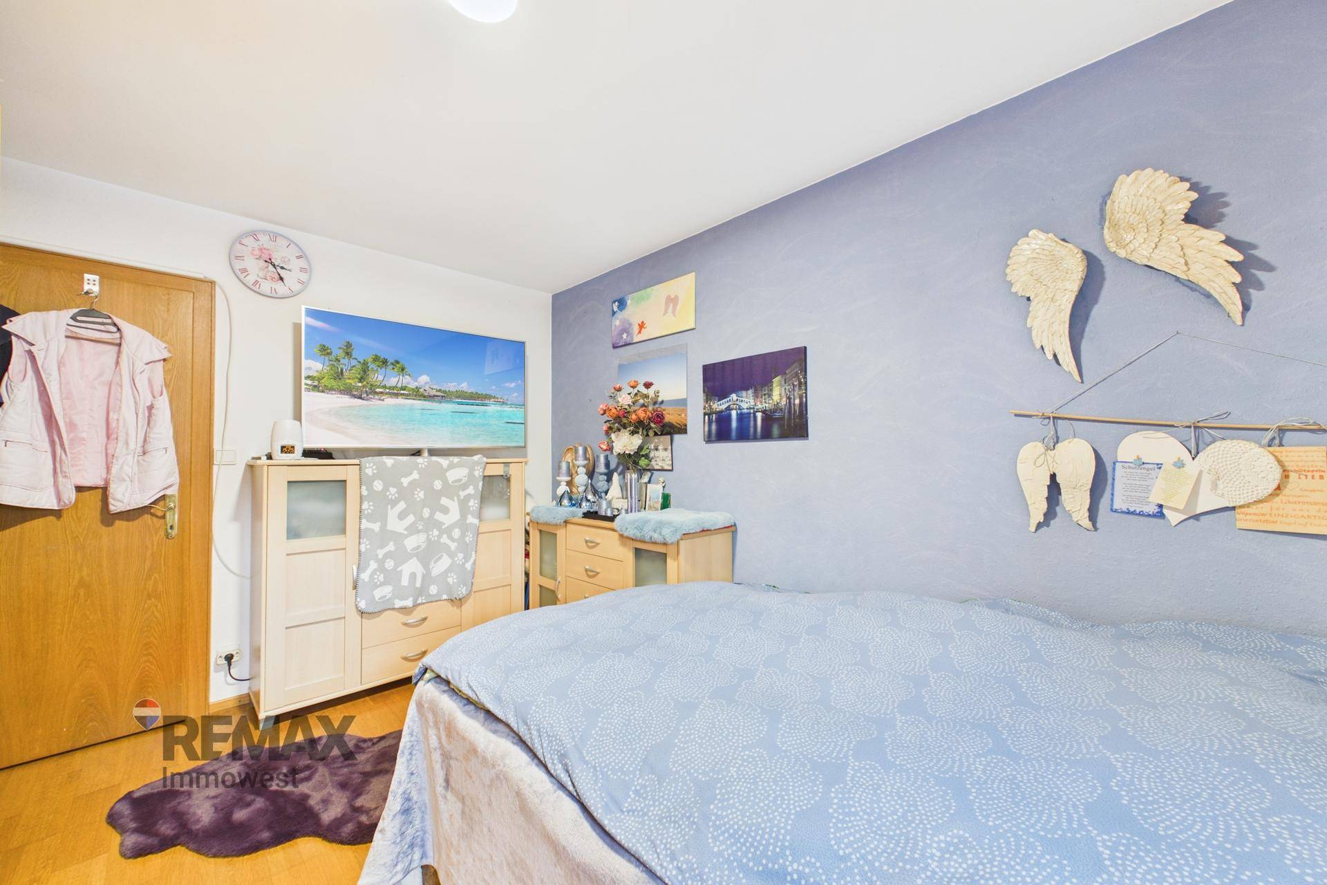 Schlafzimmer mit blauer Wand, Holzboden und einem Fernseher auf einer Kommode.