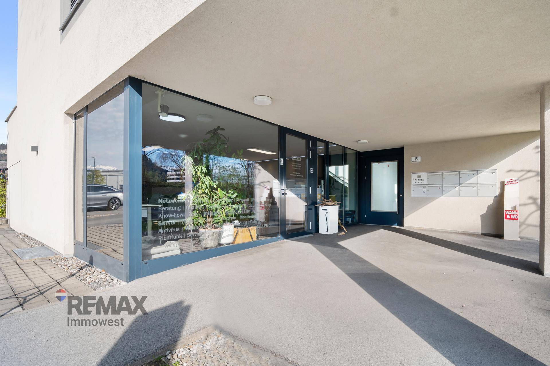 Eingangsbereich eines modernen Geschäftsgebäudes mit großen Glasfronten und Zugang zum Innenbereich.