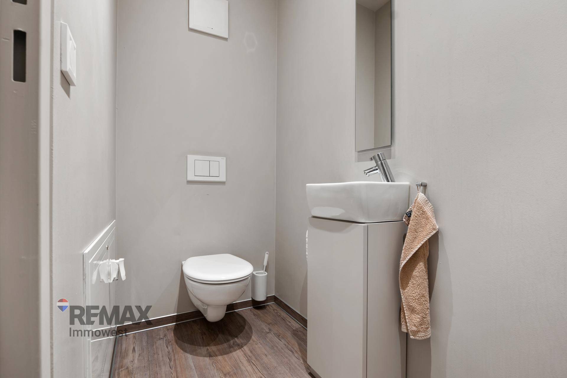 Modernes Gäste-WC mit wandhängender Toilette, kleinem Waschbecken und dunklem Holzfußboden.