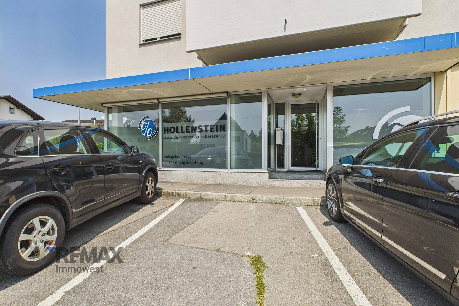 Vorderansicht des Gebäudeeingangs mit Parkplätzen und einer blauen Markise.