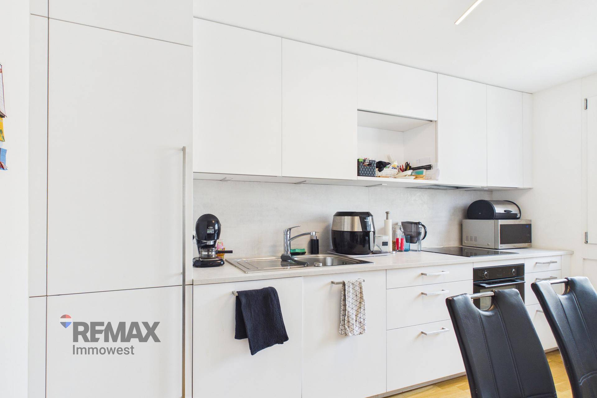 Moderne weiße Küche mit integrierten Geräten und minimalistischem Design.