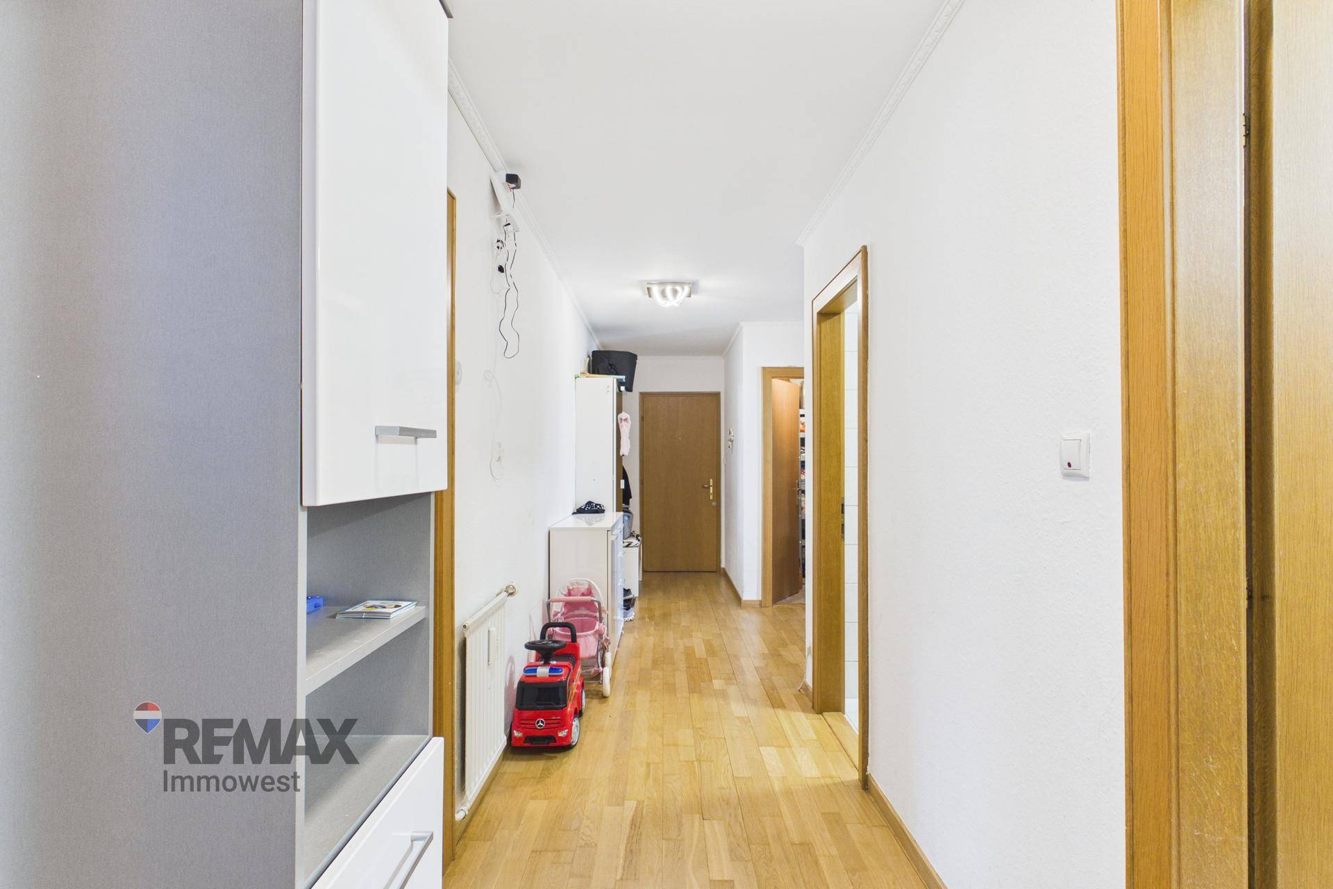 Langer, heller Flur mit Holzfußboden und Stauraum, der verschiedene Zimmer verbindet.