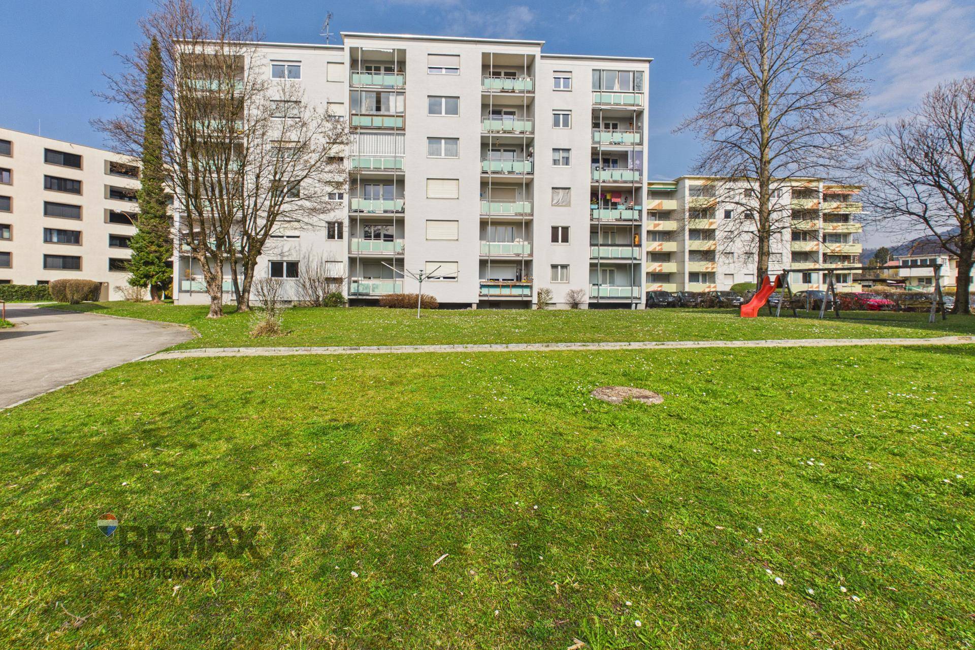 Wohngebäude mit Grünflächen und einem kleinen Spielplatz im Vordergrund.