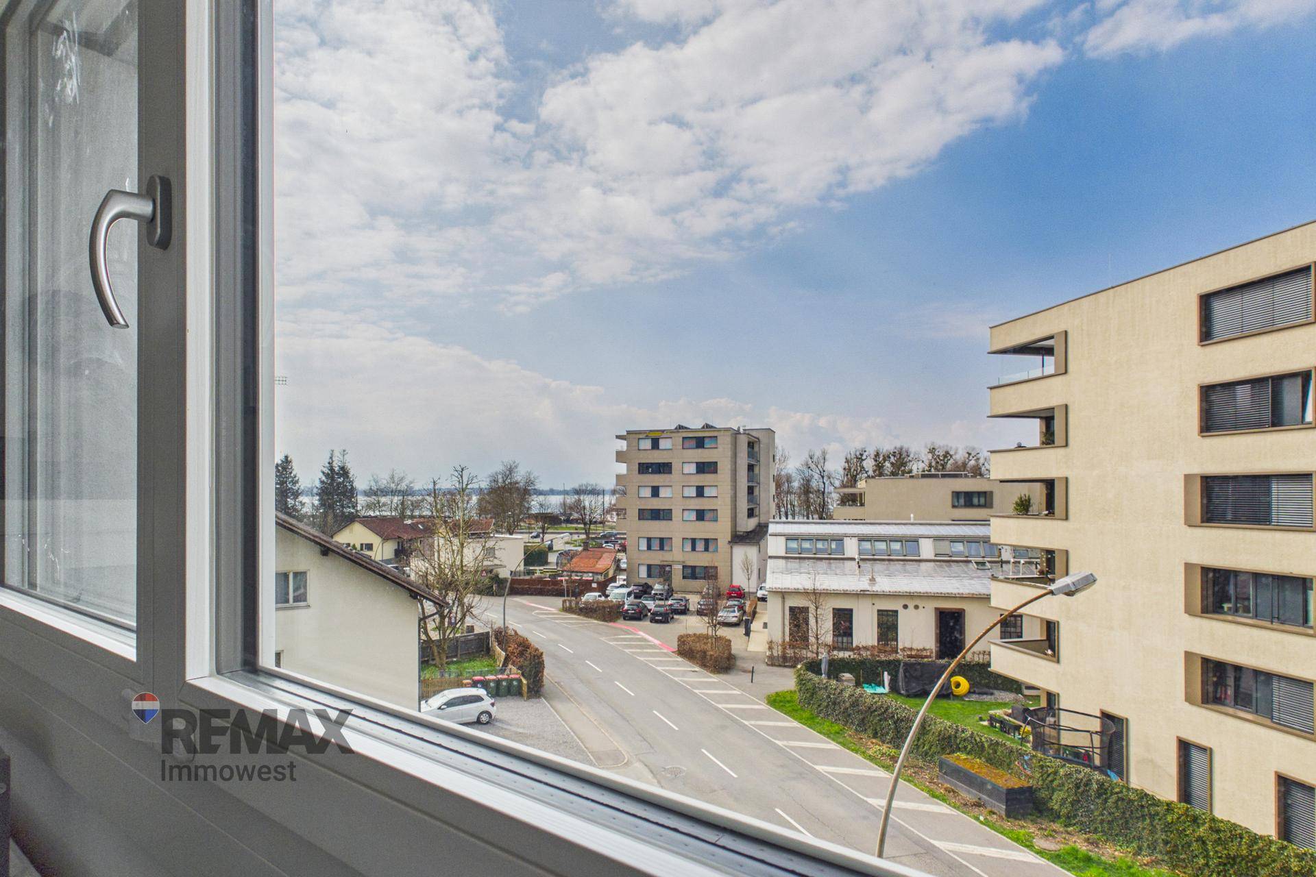 Weitblick aus dem Fenster über die Stadt, mit See und Bergen am Horizont.