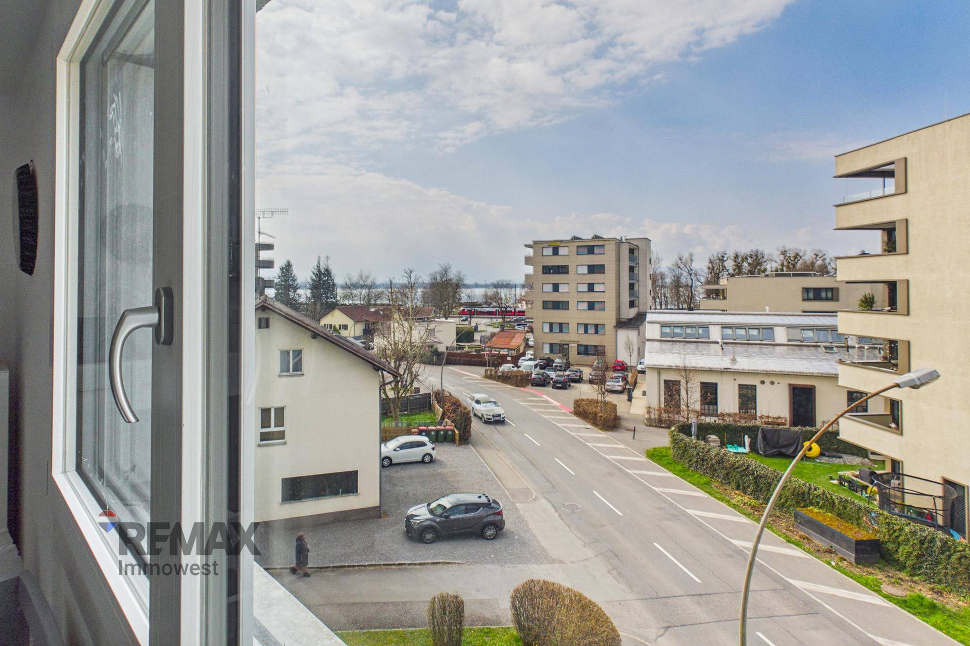 Ausblick aus dem Fenster auf die Straße, umliegende Gebäude und einen See in der Ferne.