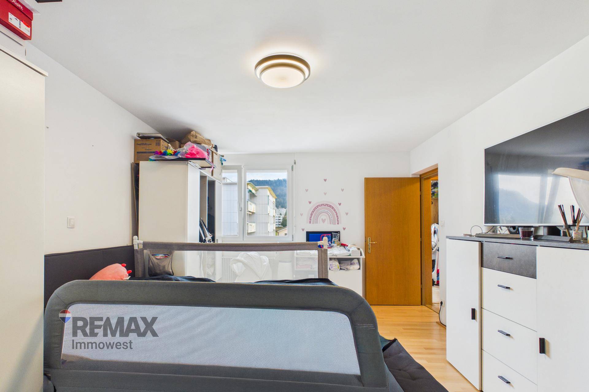 Helles Schlafzimmer mit Holzfußboden, Fenster und Blick auf die grüne Umgebung.