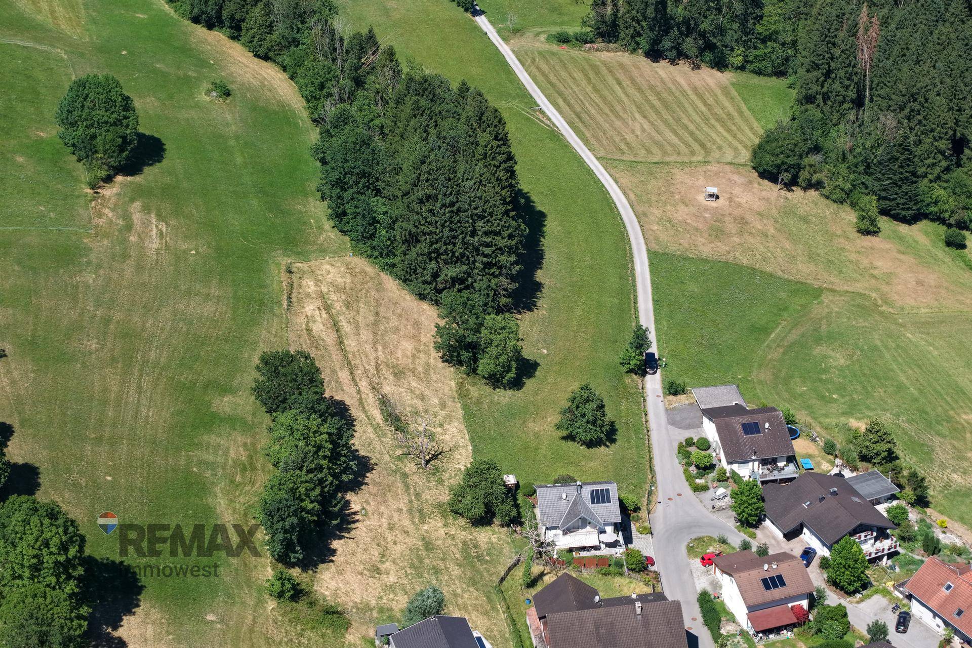 Luftaufnahme von Wohnhäusern am Rande grüner Felder und Wälder mit einer kurvigen Straße.