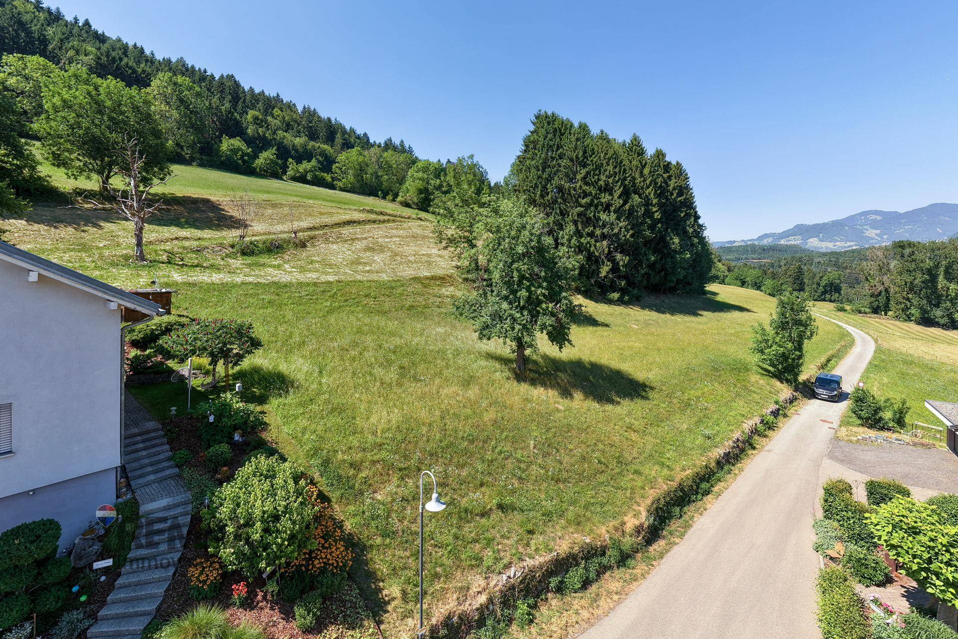 Blick auf ein Wohnhaus mit einem liebevoll angelegten Garten und einer Zufahrtsstraße am Hang.