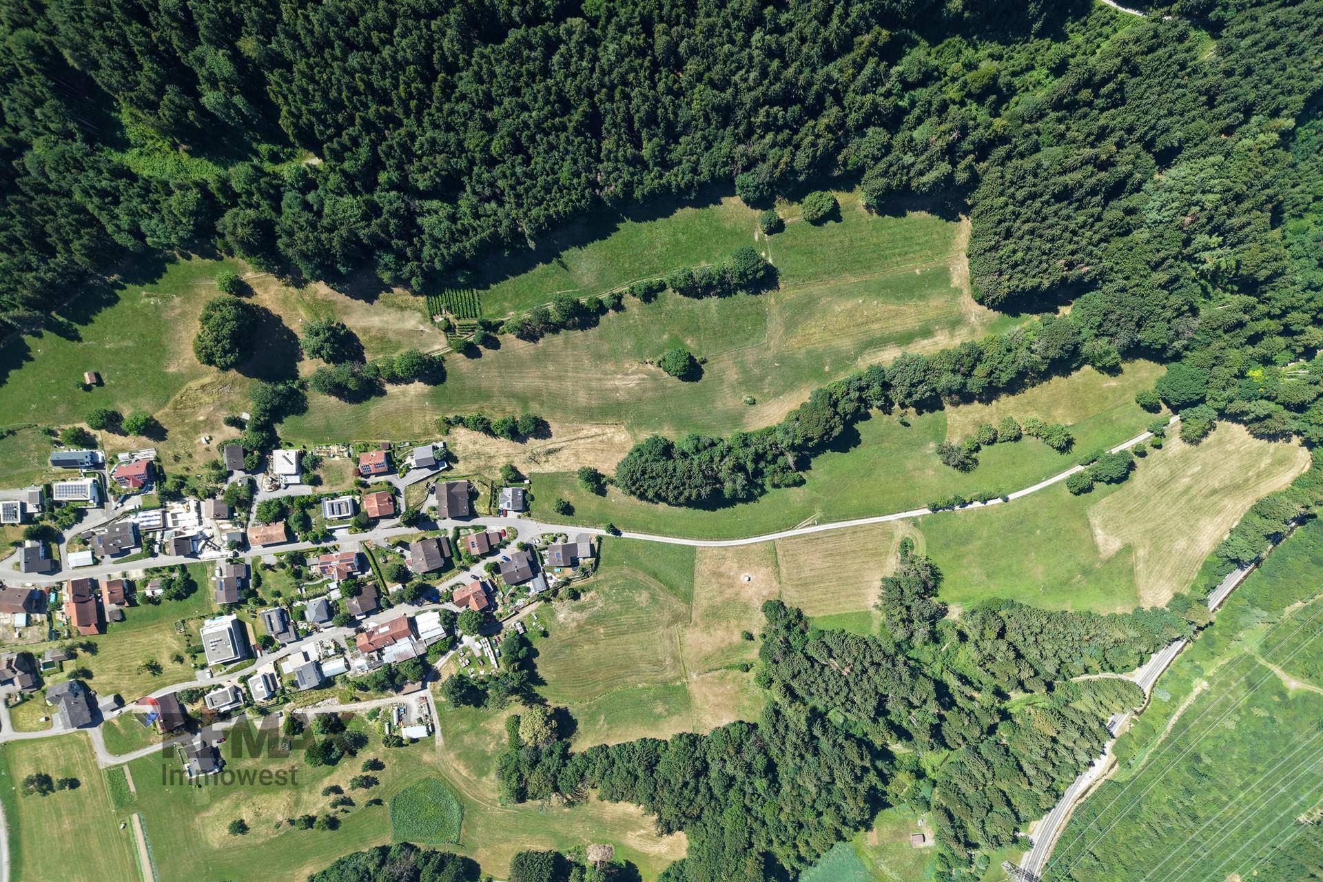 Weitläufige Luftaufnahme eines kleinen Dorfes, eingebettet in grüne Felder und dichte Wälder.