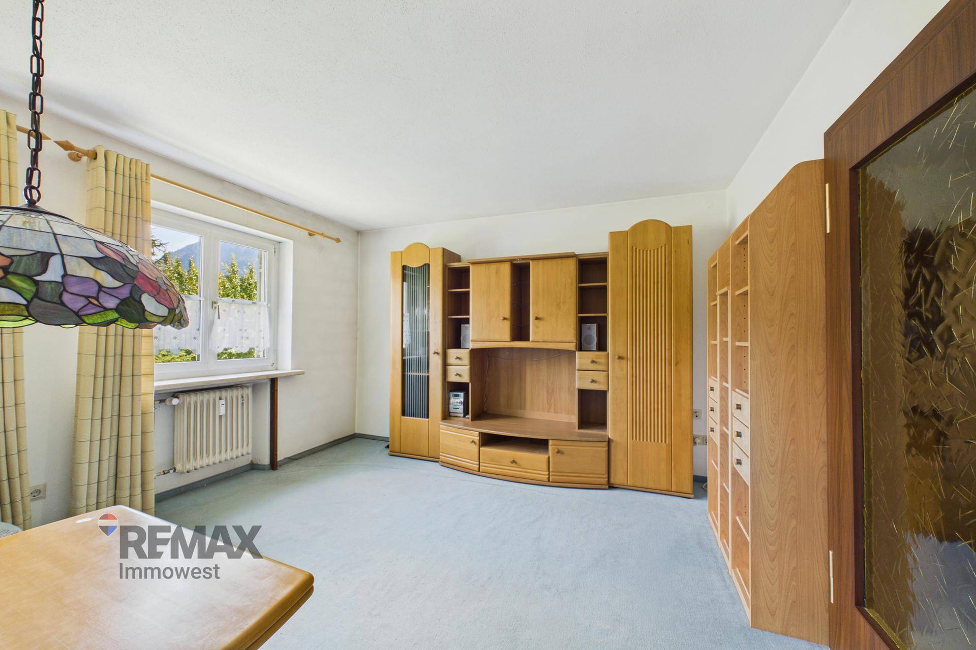 Helles Wohnzimmer mit Teppichboden und einer großen Holzschrankwand, die viel Stauraum bietet.