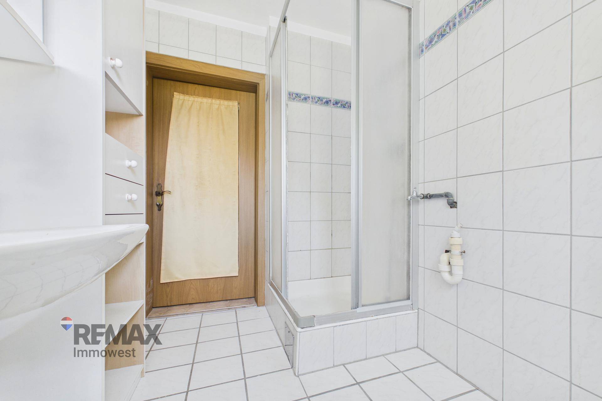 Badezimmer mit Duschkabine, weißen Fliesen und einem praktischen Regal für Badutensilien.