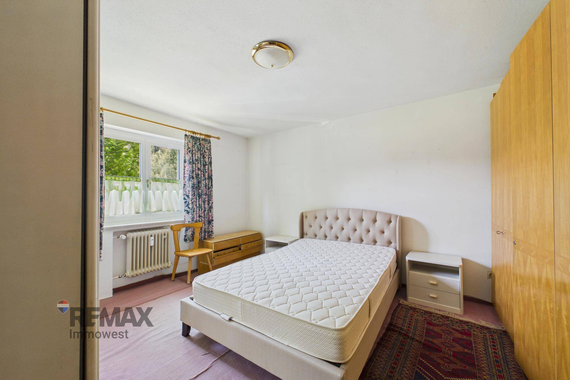 Schlafzimmer mit Doppelbett, Nachttischen und einem Fenster mit Blick auf die grüne Umgebung.