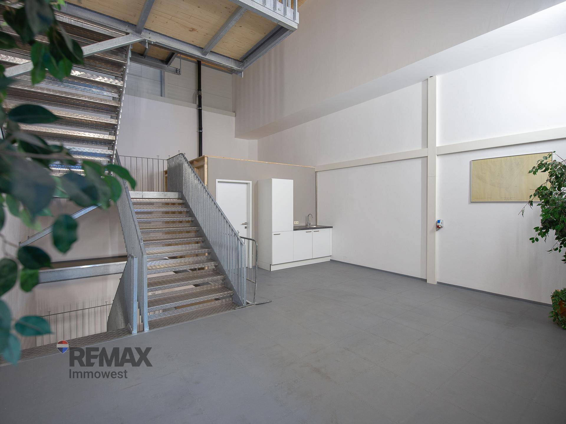 Offener Bereich mit einer modernen Metalltreppe und einer kleinen Küchenzeile, umgeben von hellen Wänden.