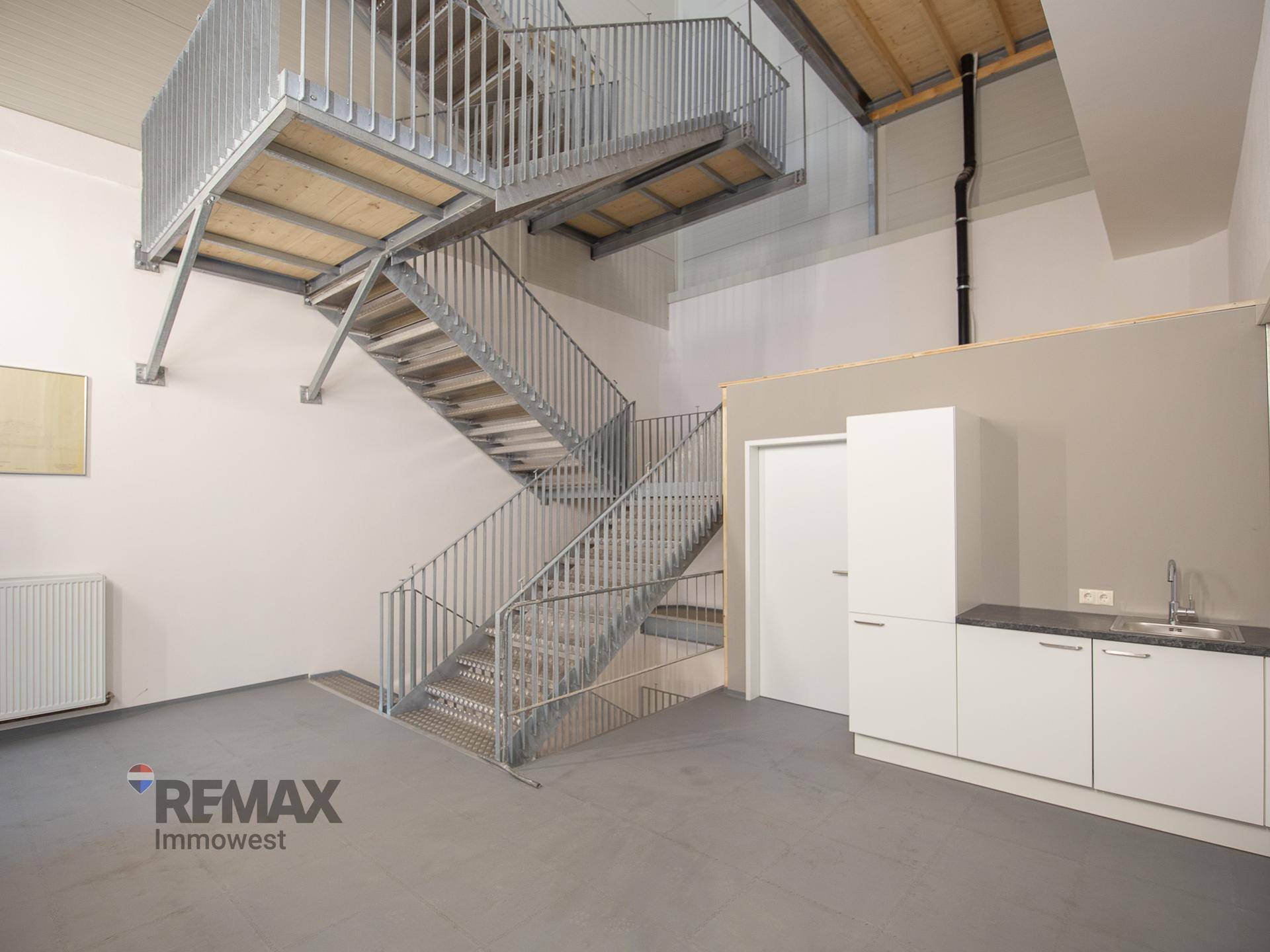 Industriell anmutende Metalltreppe führt zu einer oberen Ebene, daneben eine funktionale Küchenzeile.