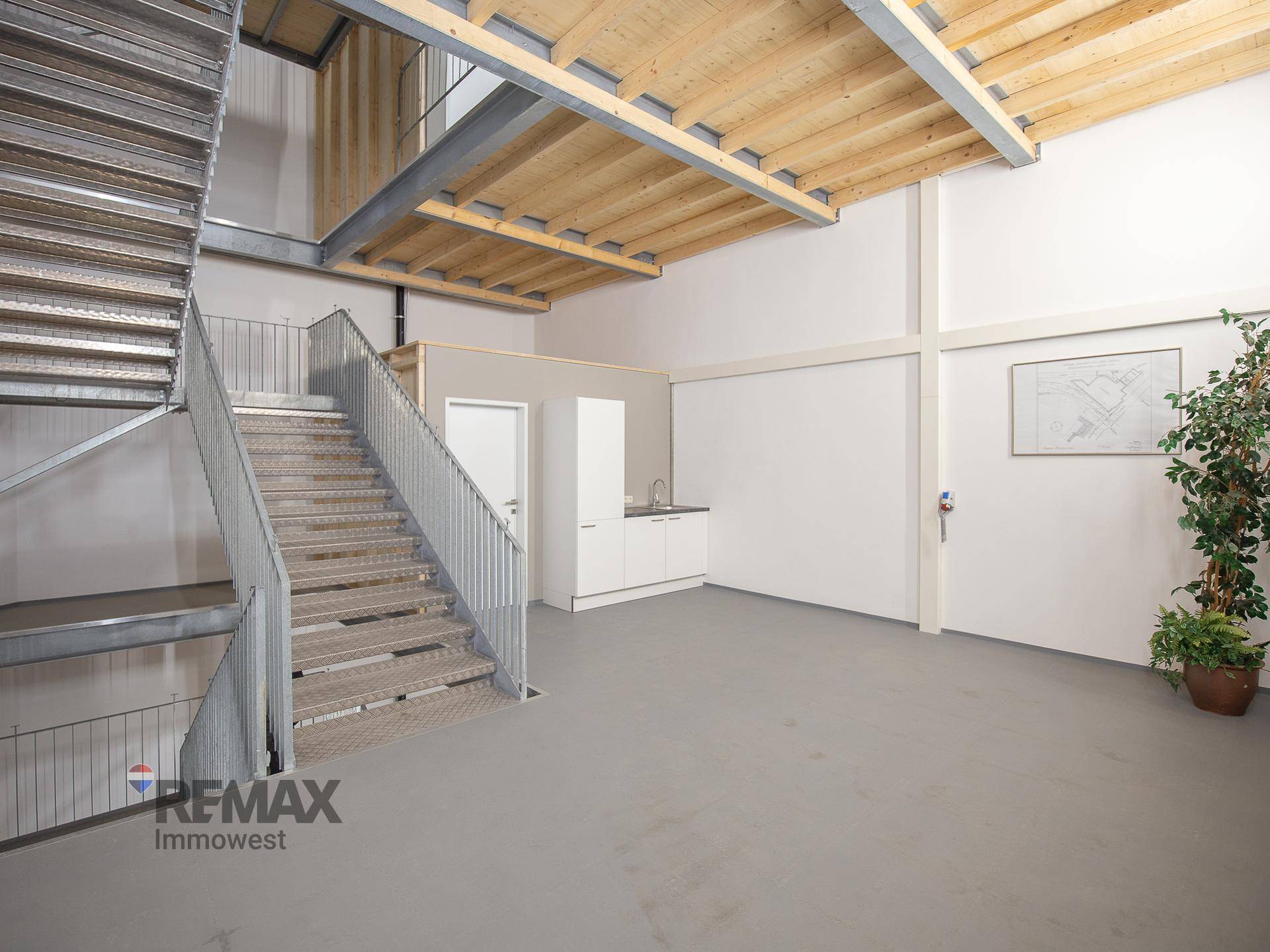 Offener Raum mit einer Metalltreppe, einer Küchenzeile und einer sichtbaren Holzdeckenkonstruktion.
