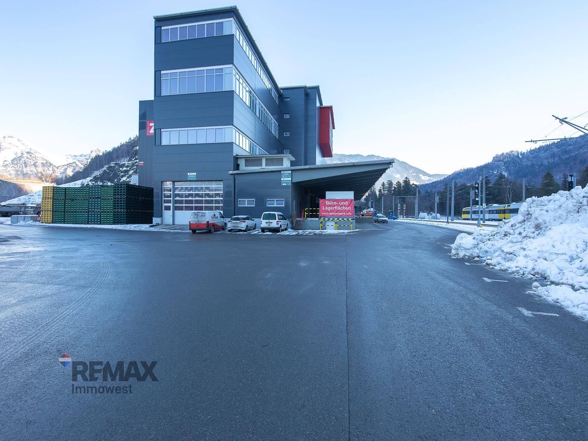Modernes Industriegebäude mit großen Fenstern und Laderampen, umgeben von Schnee und Bergen im Winter.