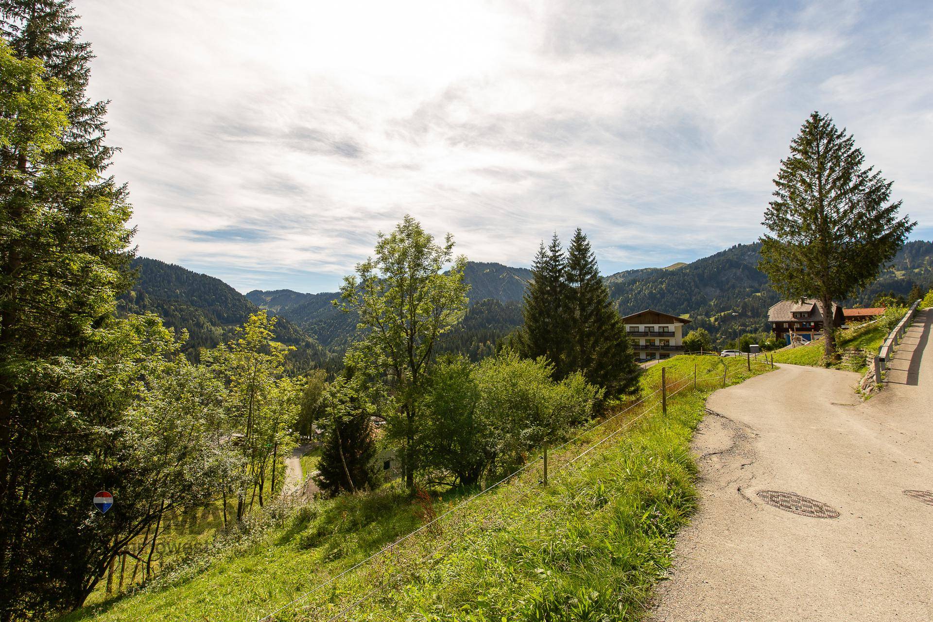 Weitläufige Aussicht auf bewaldete Berge und Gebäude entlang eines kurvigen Weges.