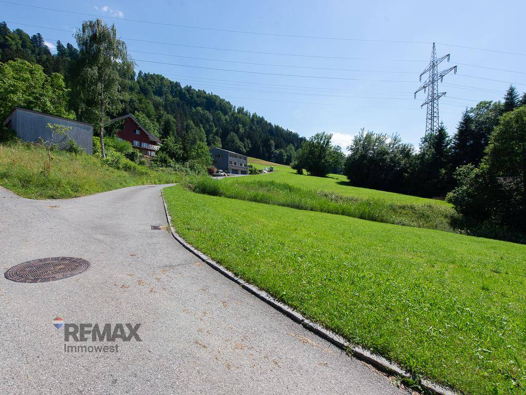 Geschwungene Landstraße mit weitem Blick über grüne Hügel und Häuser in der Ferne.